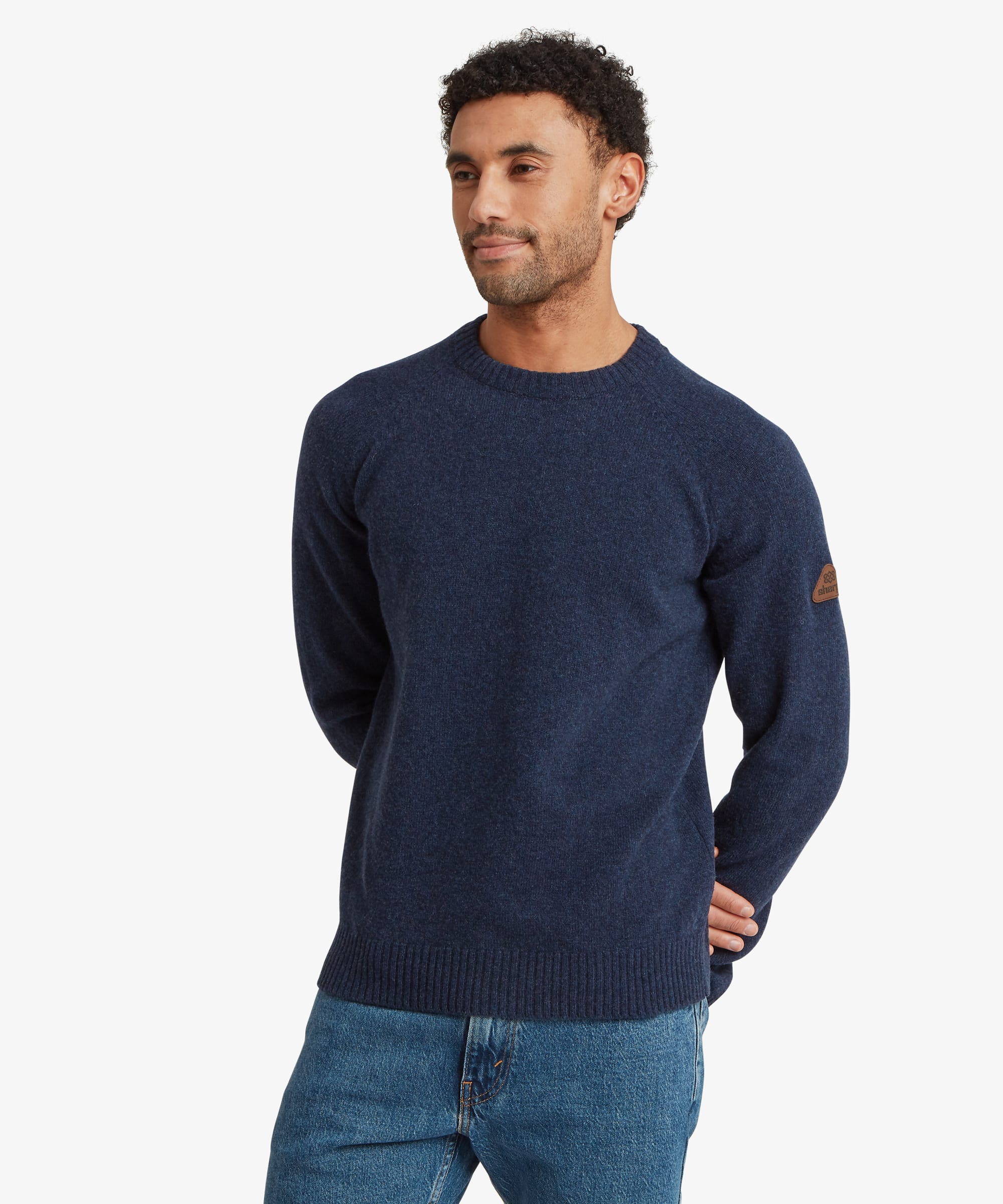 Male model wearing the Sherpa Kangtega Crew Sweater in blue with dark blue jeans, shown from the front. The sweater features a timeless crew neckline, long sleeves, ribbed cuffs and hem, and a clean regular fit.