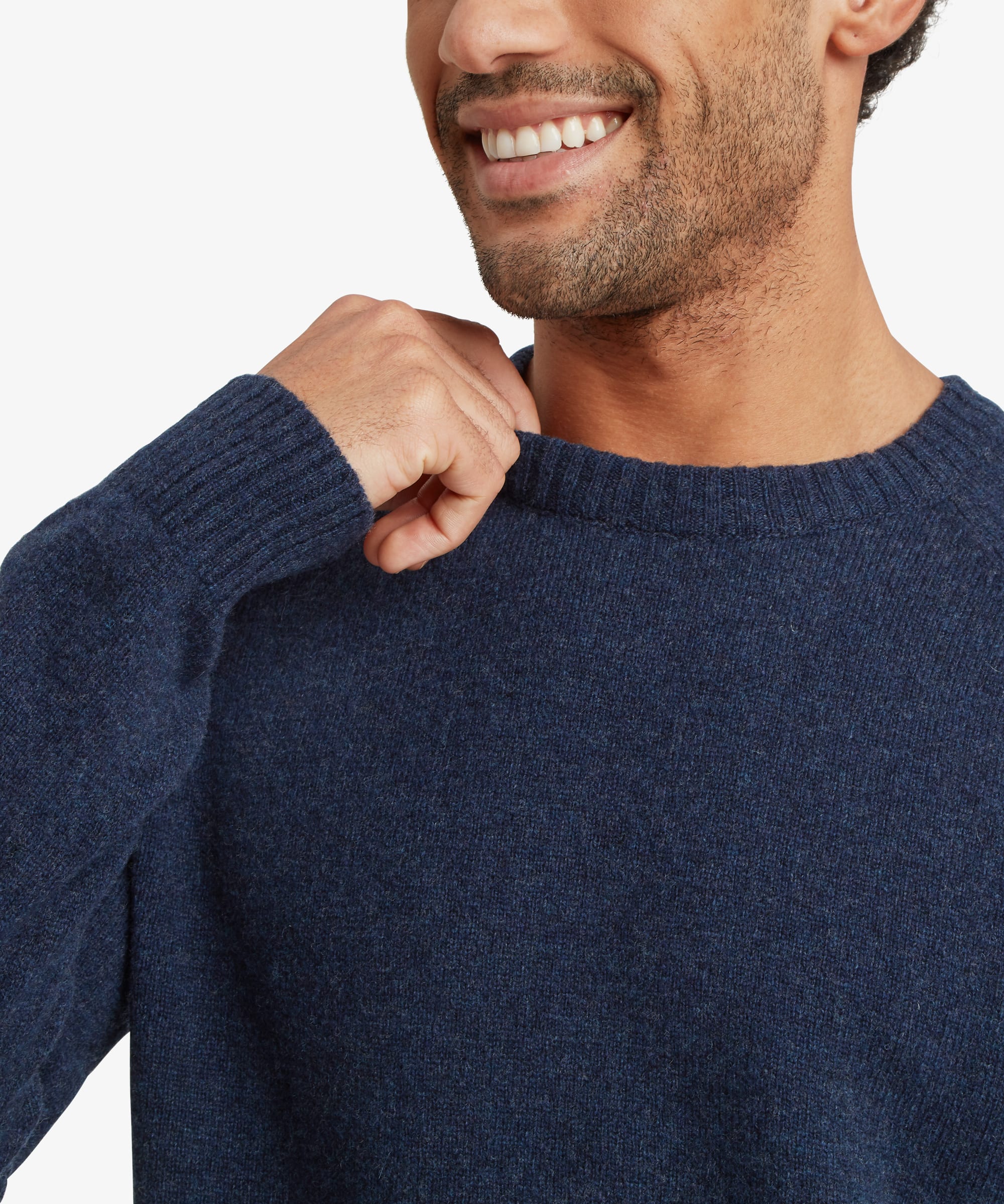 Close-up of a man wearing a navy blue knit crewneck sweater, showing the texture of the fabric and the ribbed collar.