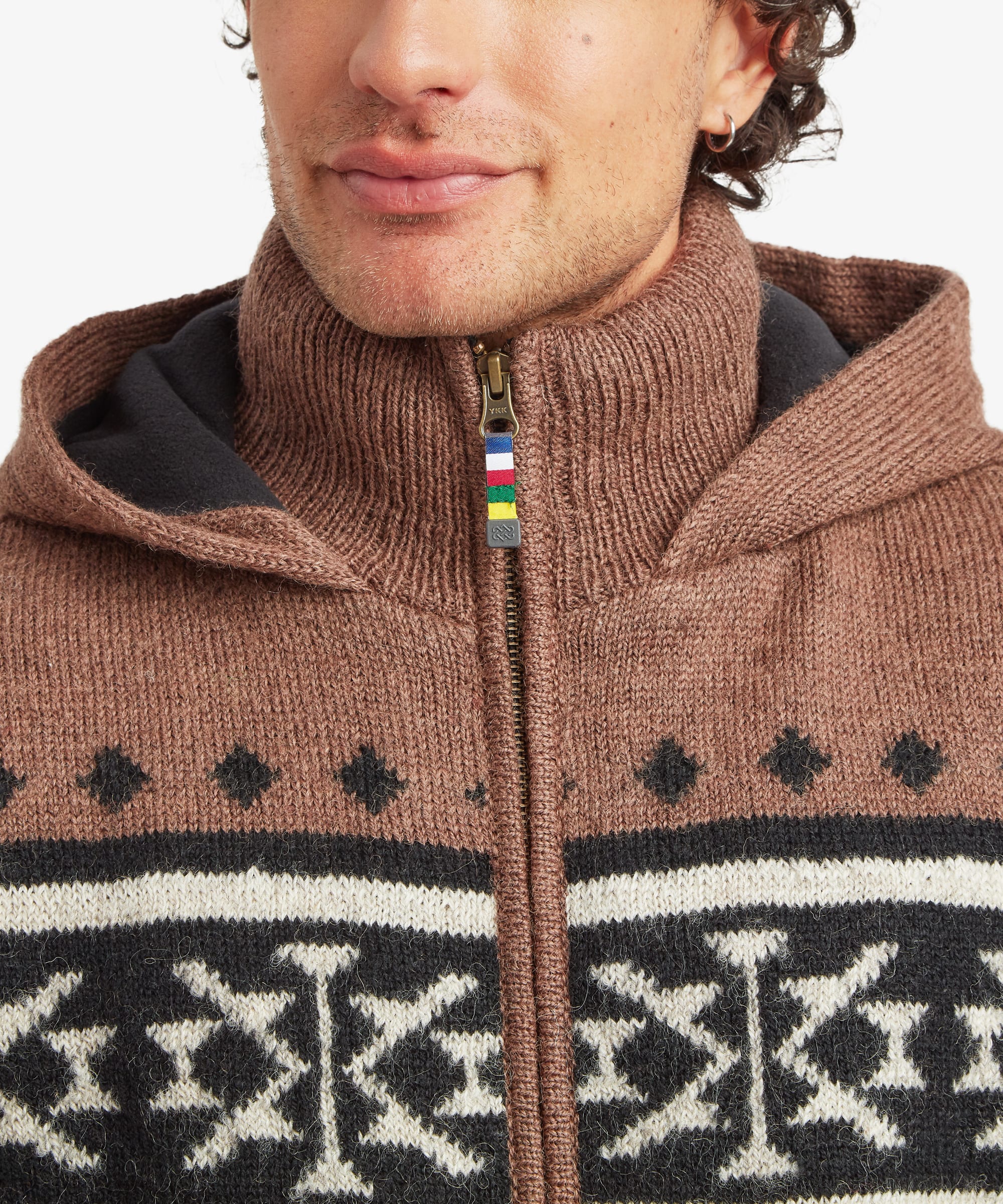 Close-up of a man wearing a brown knit zip-up hoodie with a black and cream geometric pattern and a small multicolor zipper pull.