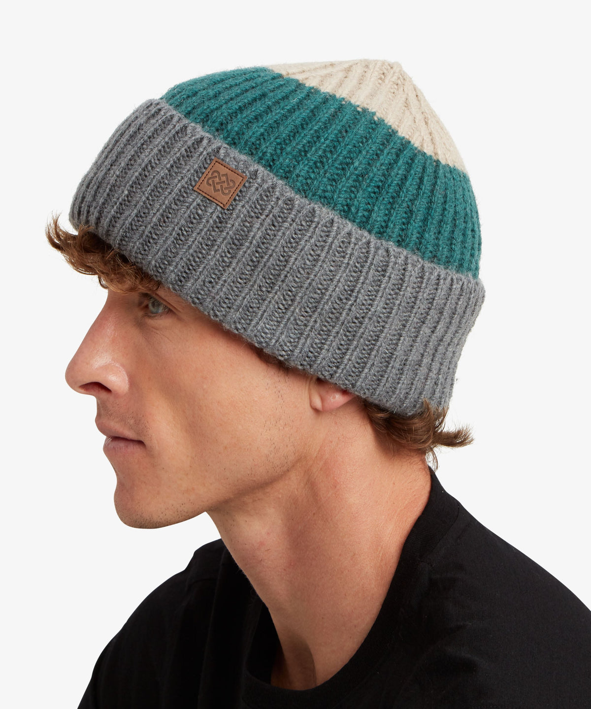 A man in profile wearing a three-stripe knit beanie with cream, teal.