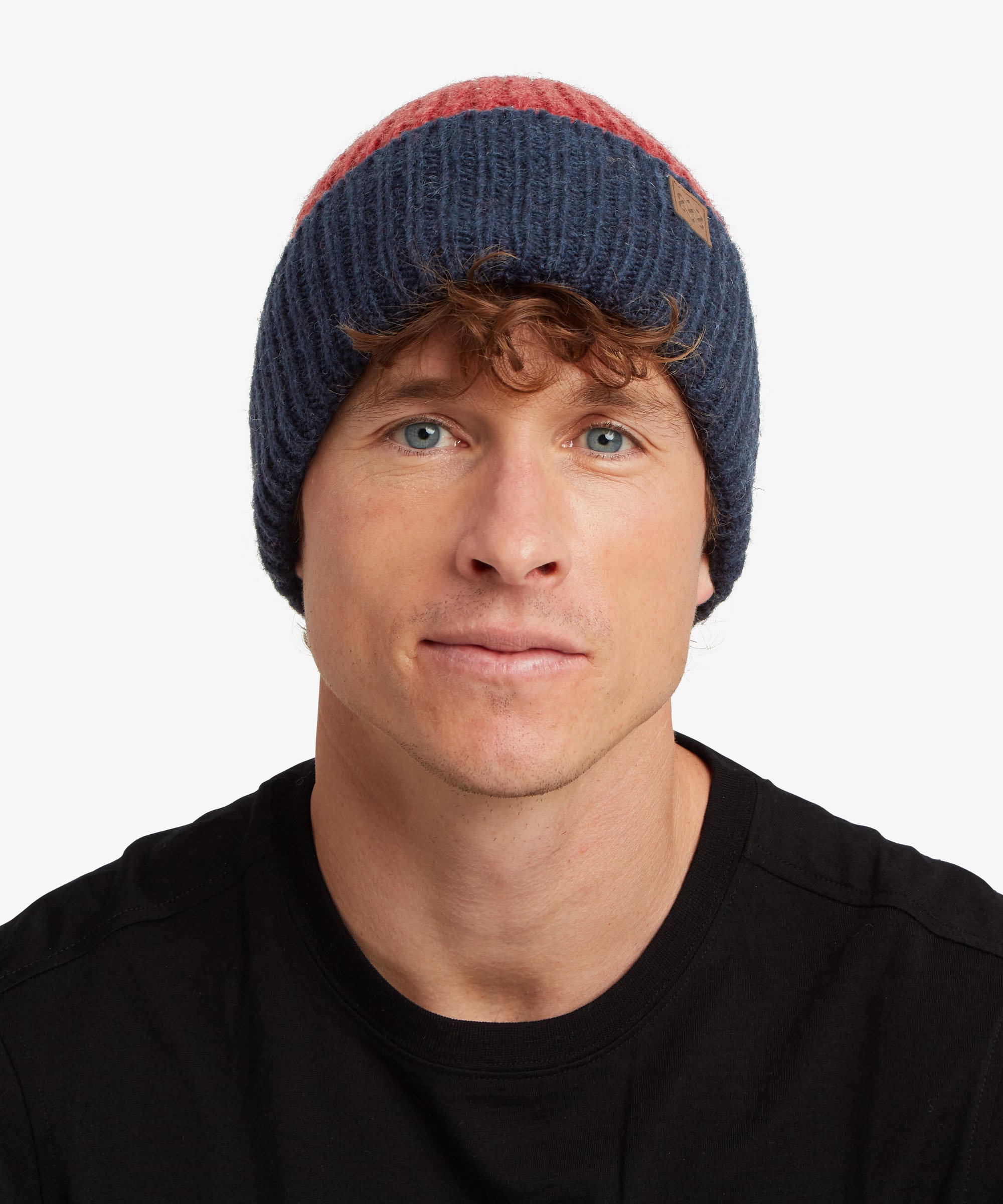 A man wearing a navy blue and red ribbed knit beanie hat, photographed against a clean light gray background.