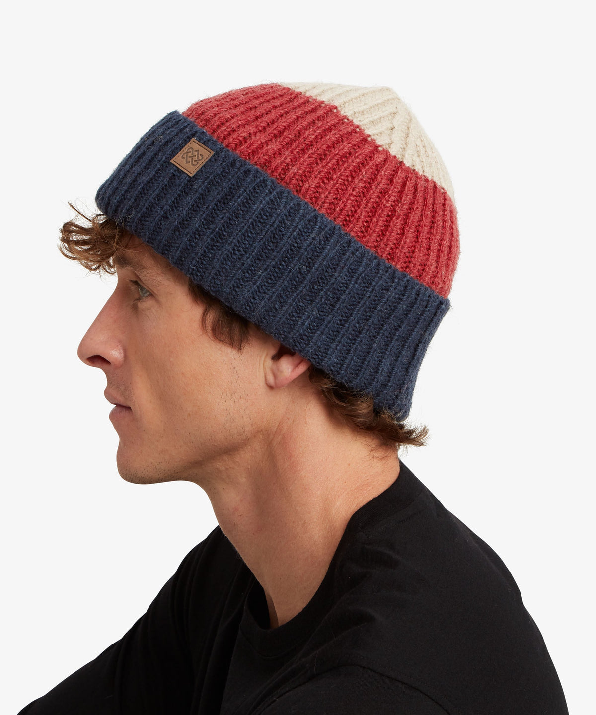 A man in profile wearing a ribbed knit beanie hat with horizontal stripes of cream, red.