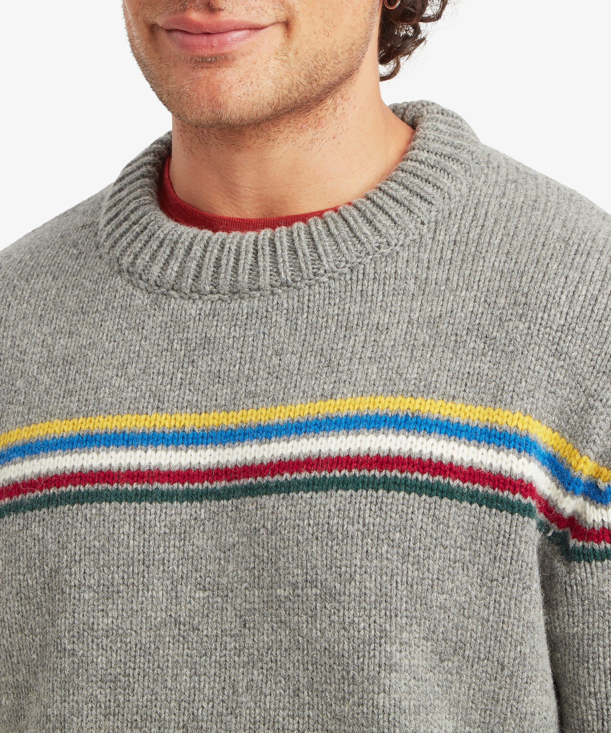 Close-up of a male model wearing the Sherpa Mahesh Sweater in grey, highlighting the soft knit texture, ribbed crew neckline and colourful striped chest detail.