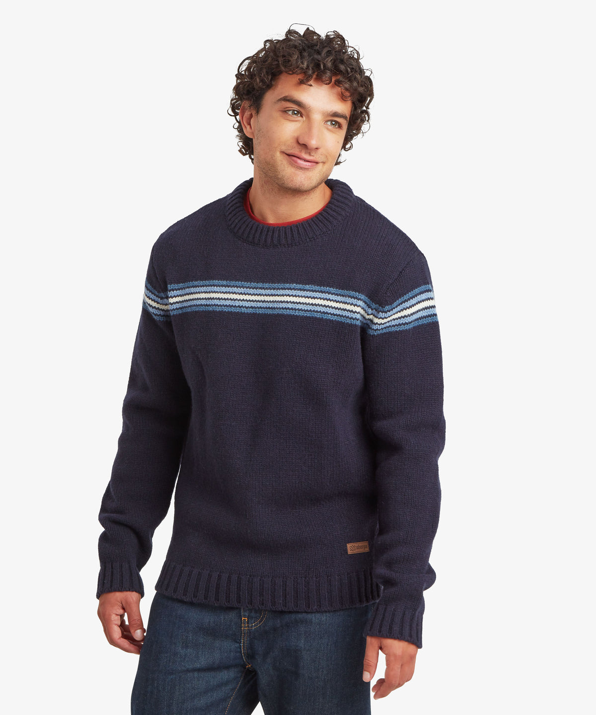 Man wearing a navy knit sweater with light blue, white and gray chest stripes and jeans.