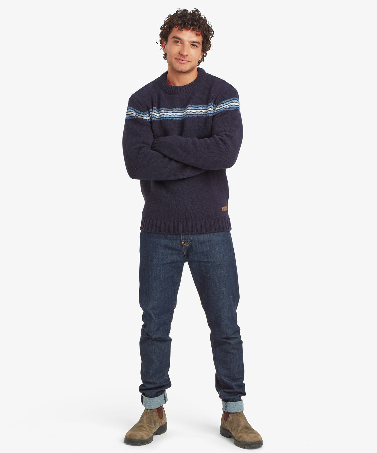 Man wearing a navy striped crewneck sweater, jeans and brown boots.