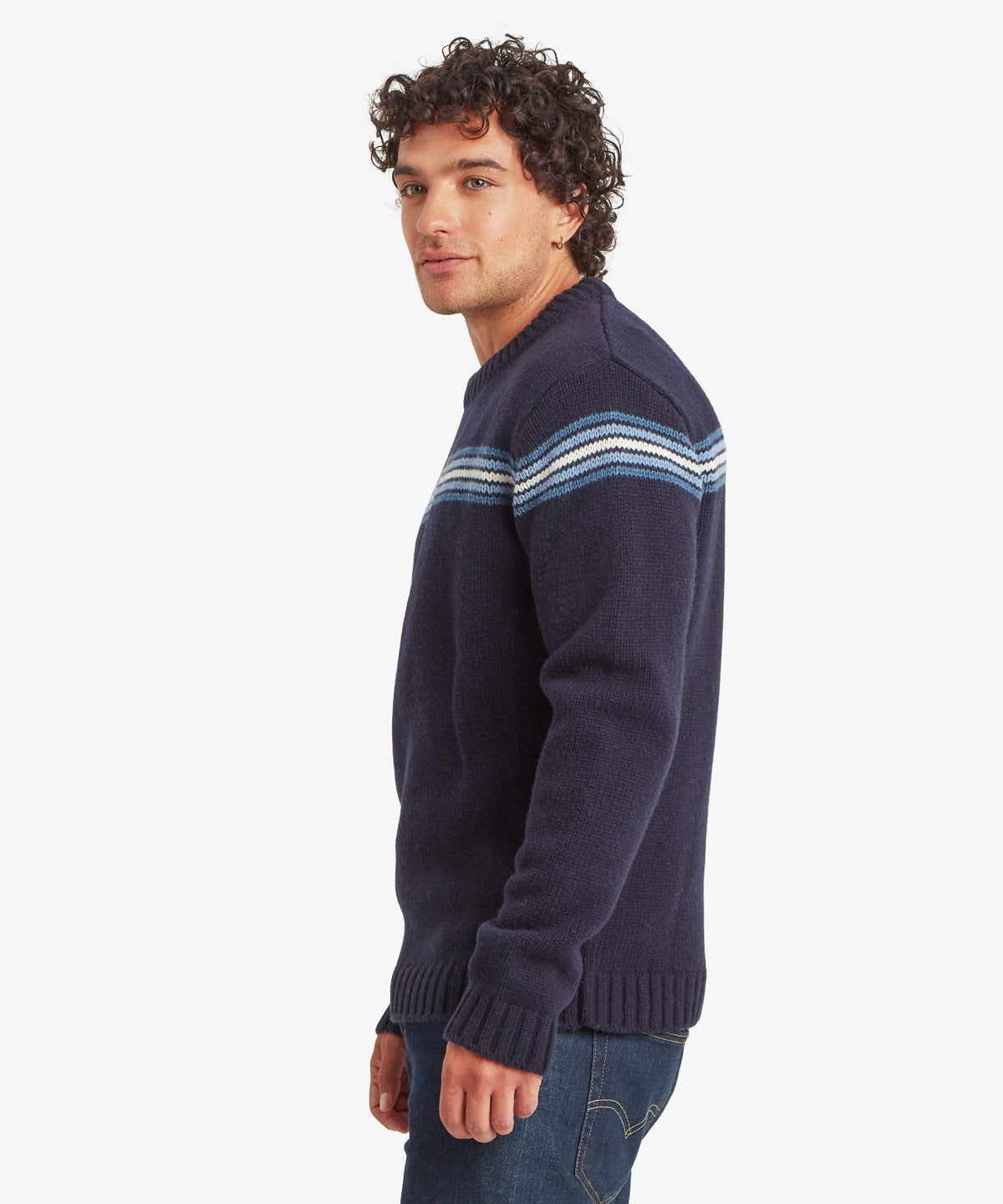 Man wearing a navy knit sweater with blue and white shoulder stripes and jeans.