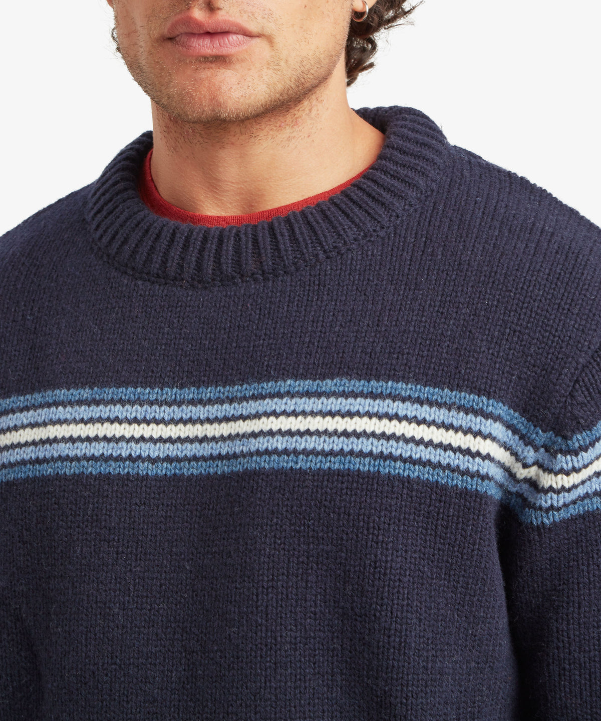 Man wearing a navy knit sweater with blue, white and red collar stripes.