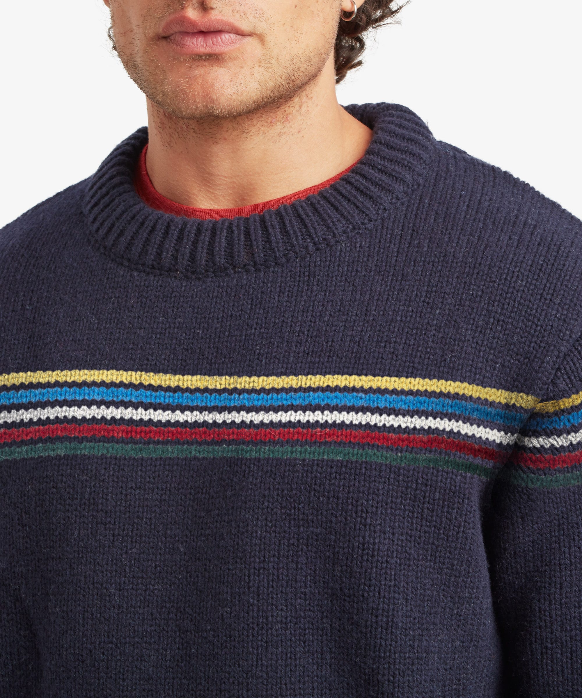 Close-up of a male model wearing the Sherpa Mahesh Sweater in blue, highlighting the soft knitted texture, ribbed crew neckline and the blue and white striped chest detail.