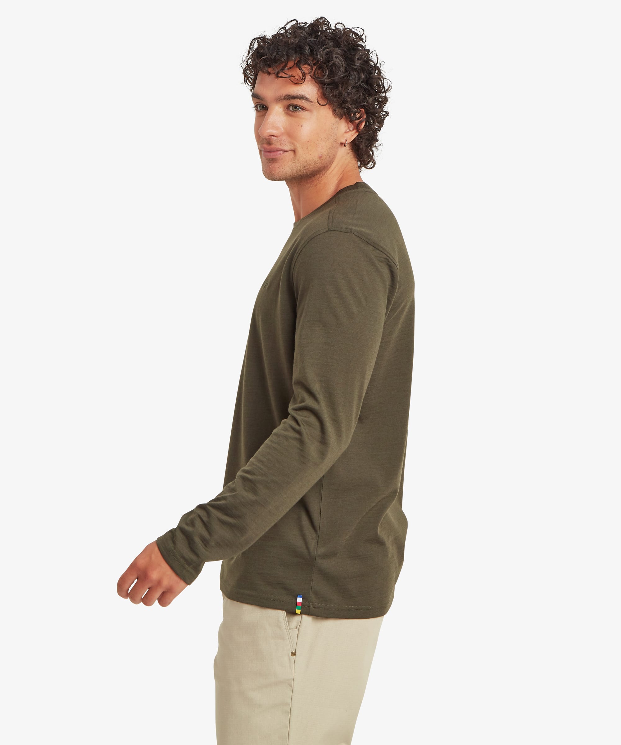 Side-profile view of a man wearing an olive green long-sleeve merino wool tee. The regular-fit silhouette, smooth fabric, and minimalist styling are shown with beige pants.