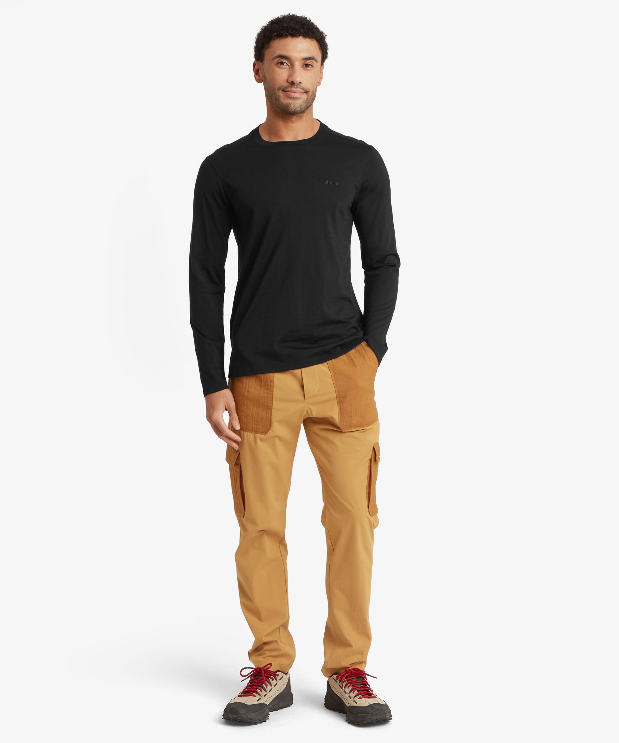 A man modeling a black long-sleeve athletic shirt and tan cargo pants with brown patch pockets, paired with red and gray sneakers, against a light gray studio background.