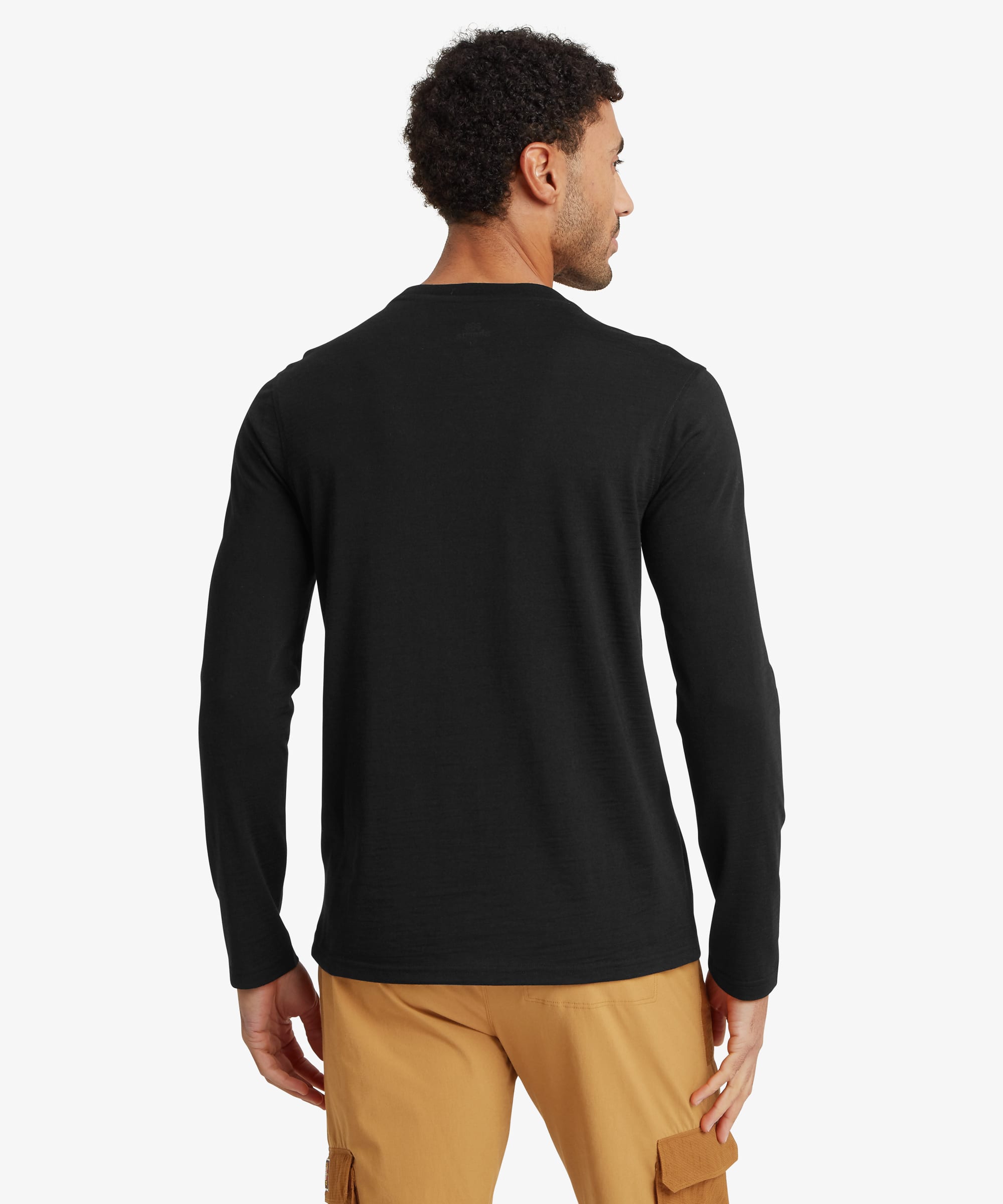 Rear view of a man wearing a black long-sleeve merino wool tee. The simple crew neck silhouette features a smooth, unadorned back and regular fit through the shoulders and body. Styled with tan pants.