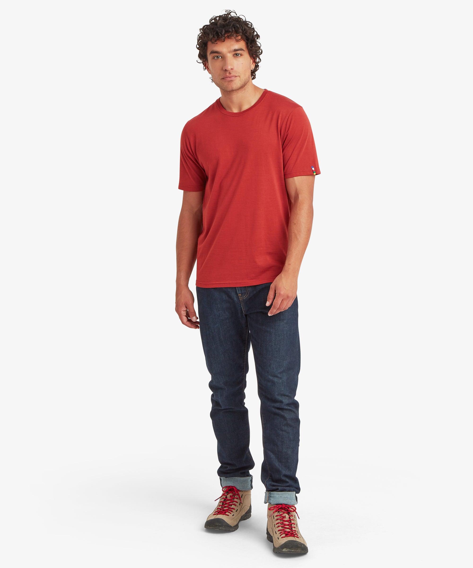 A full-length view of a rust‑red Merino wool short-sleeve T‑shirt styled with dark denim jeans and tan hiking boots with red laces.