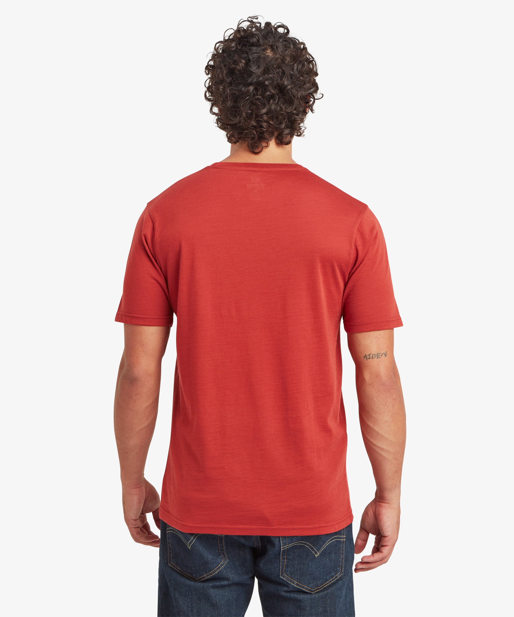 A back view of a rust‑red Merino wool short-sleeve T‑shirt styled with dark denim jeans.