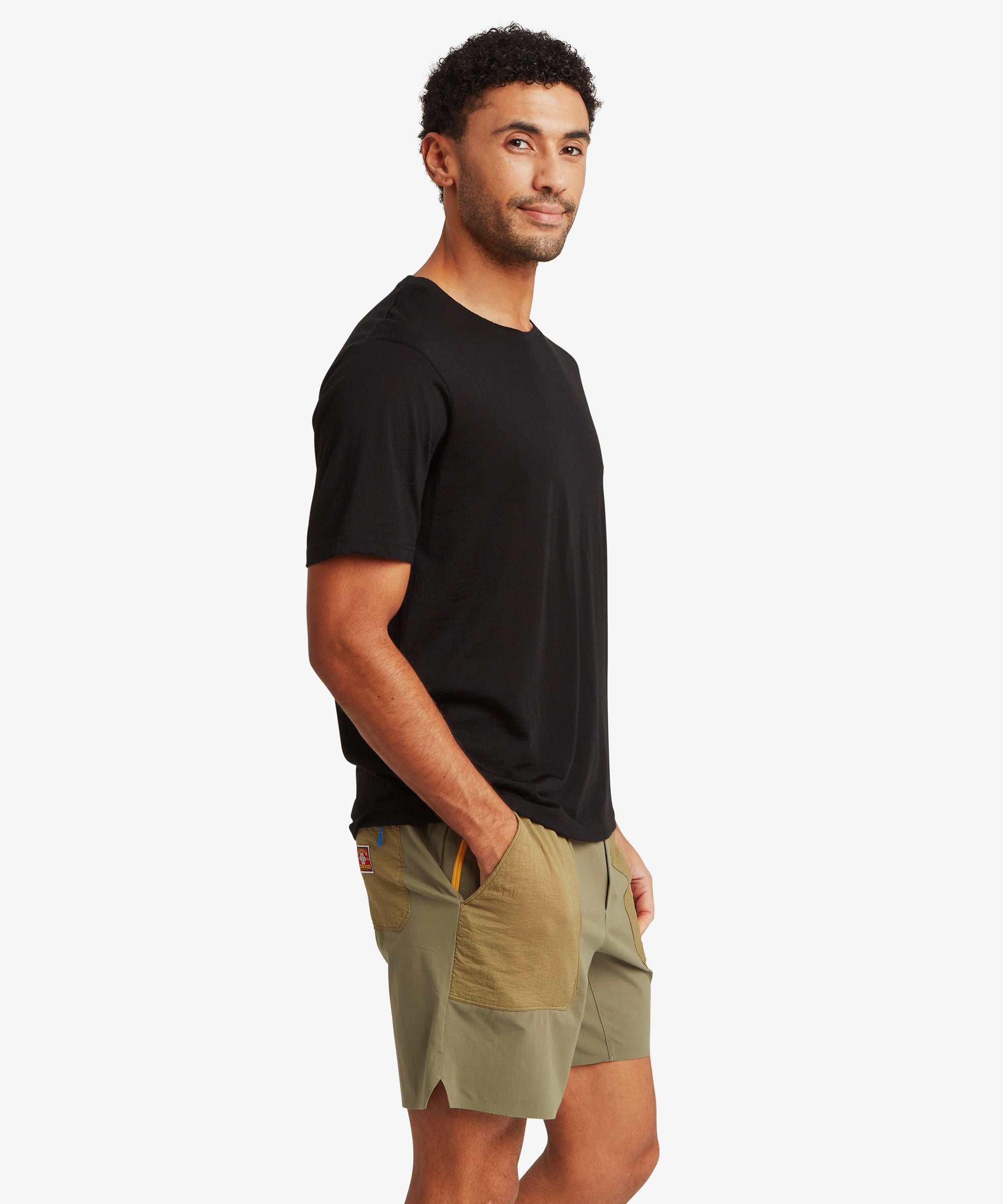 A side view of a black Merino wool T‑shirt paired with two‑tone olive outdoor shorts featuring front ripstop pockets.