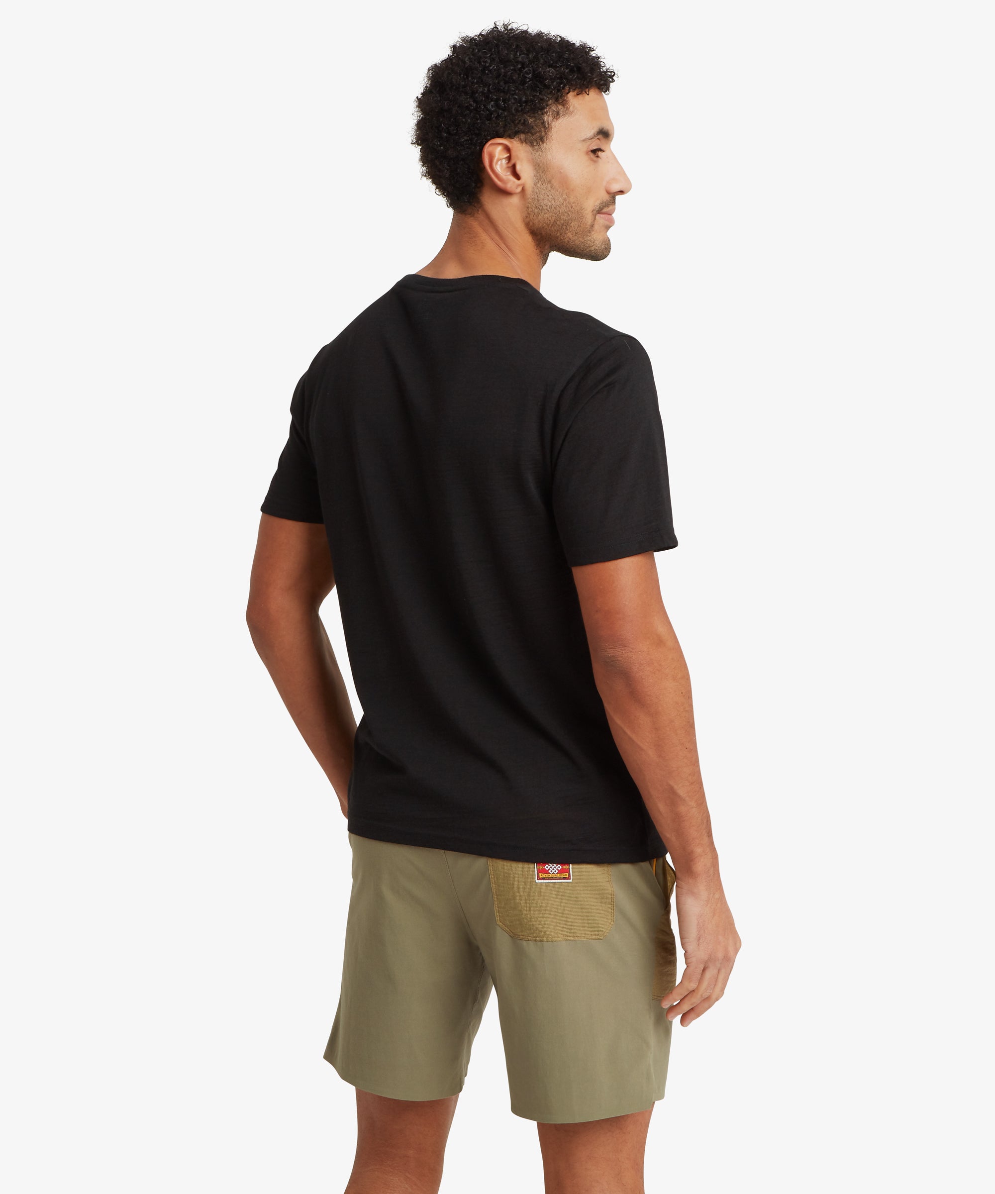 A back view of a black Merino wool short-sleeve T‑shirt paired with two‑tone olive outdoor shorts featuring a contrasting patch pocket on the back.