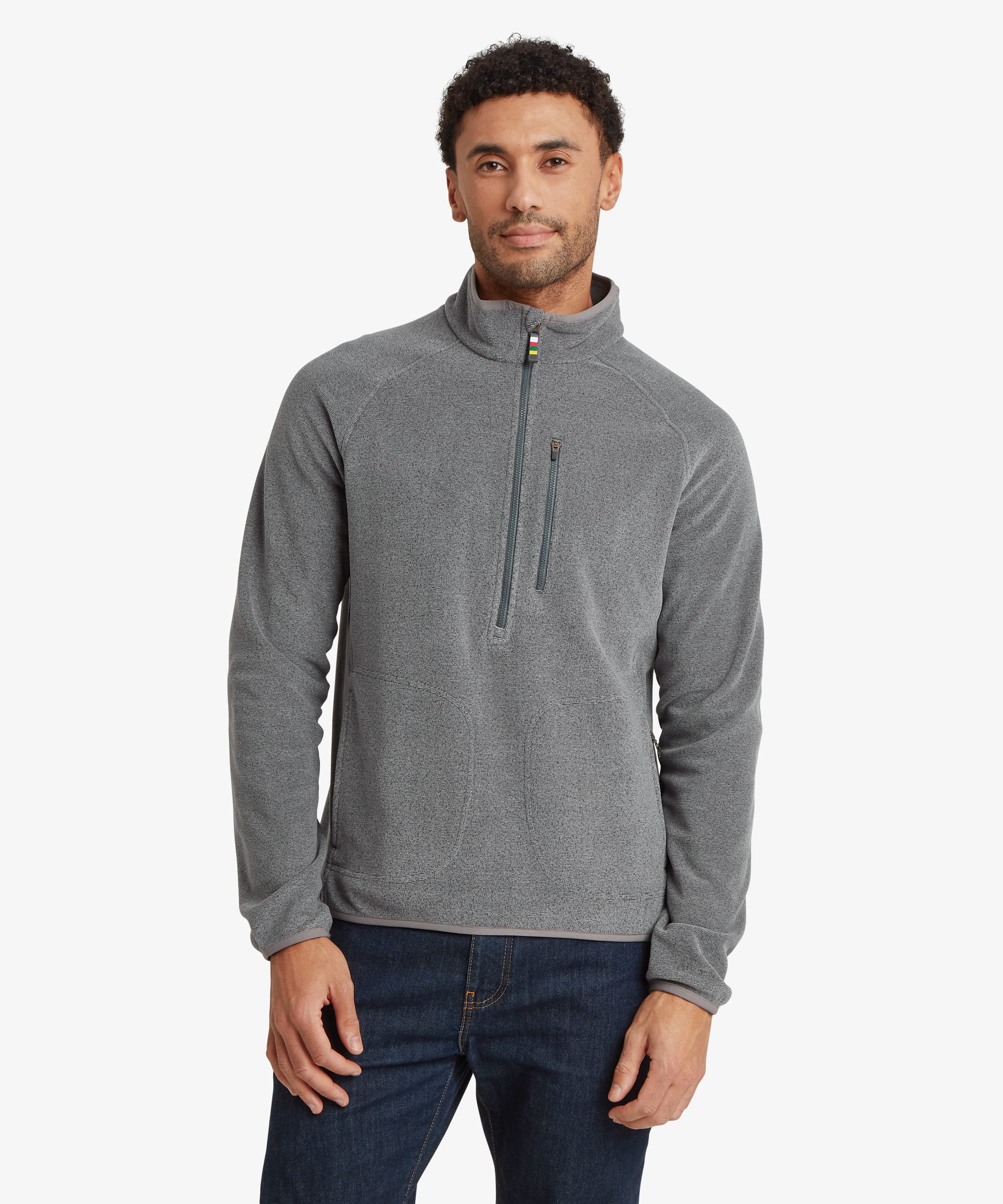 Man wearing a light grey Rolpa 1/2-zip fleece pullover with the zipper partially closed. The fleece features a stand collar, zip chest pocket, zip hand pockets, and small multicolor trim accents near the zippers. Paired with dark jeans.
