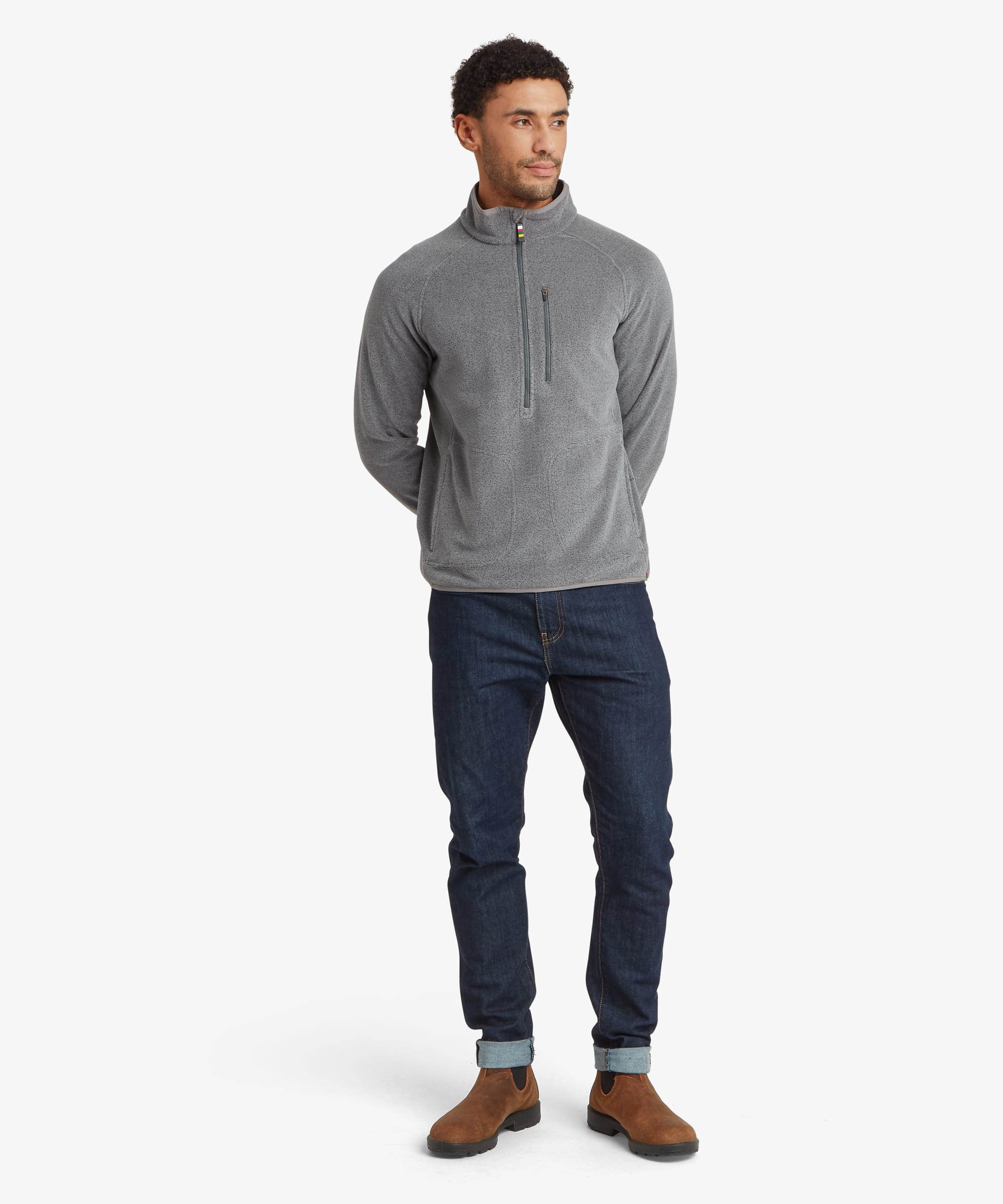 Full-body front view of the grey Rolpa 1/2-zip fleece. The regular-fit pullover features a high collar, vertical zip chest pocket, zippered hand pockets, and contrast zipper details. Styled with dark jeans and brown shoes.