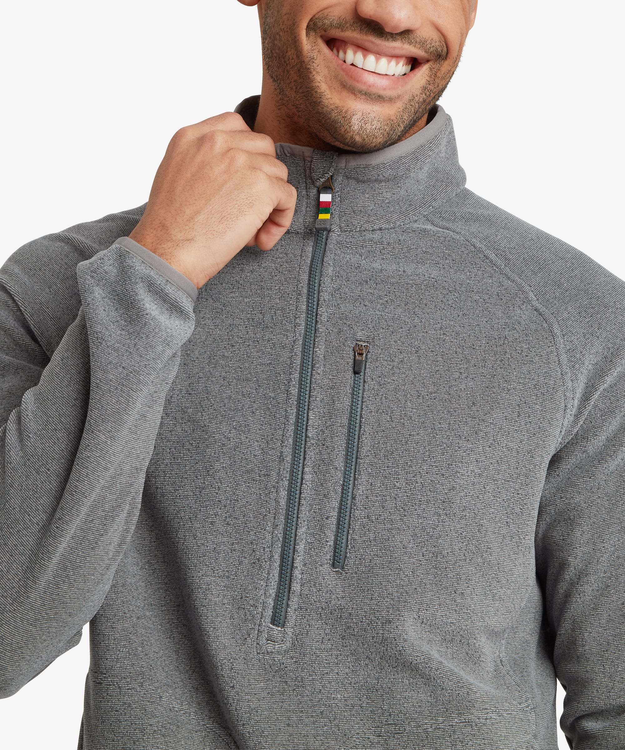 Close-up of the grey fleece pullover highlighting the high stand collar, half-zip opening with contrast zipper pull, zip chest pocket, and soft textured fabric. The model lightly holds the collar.