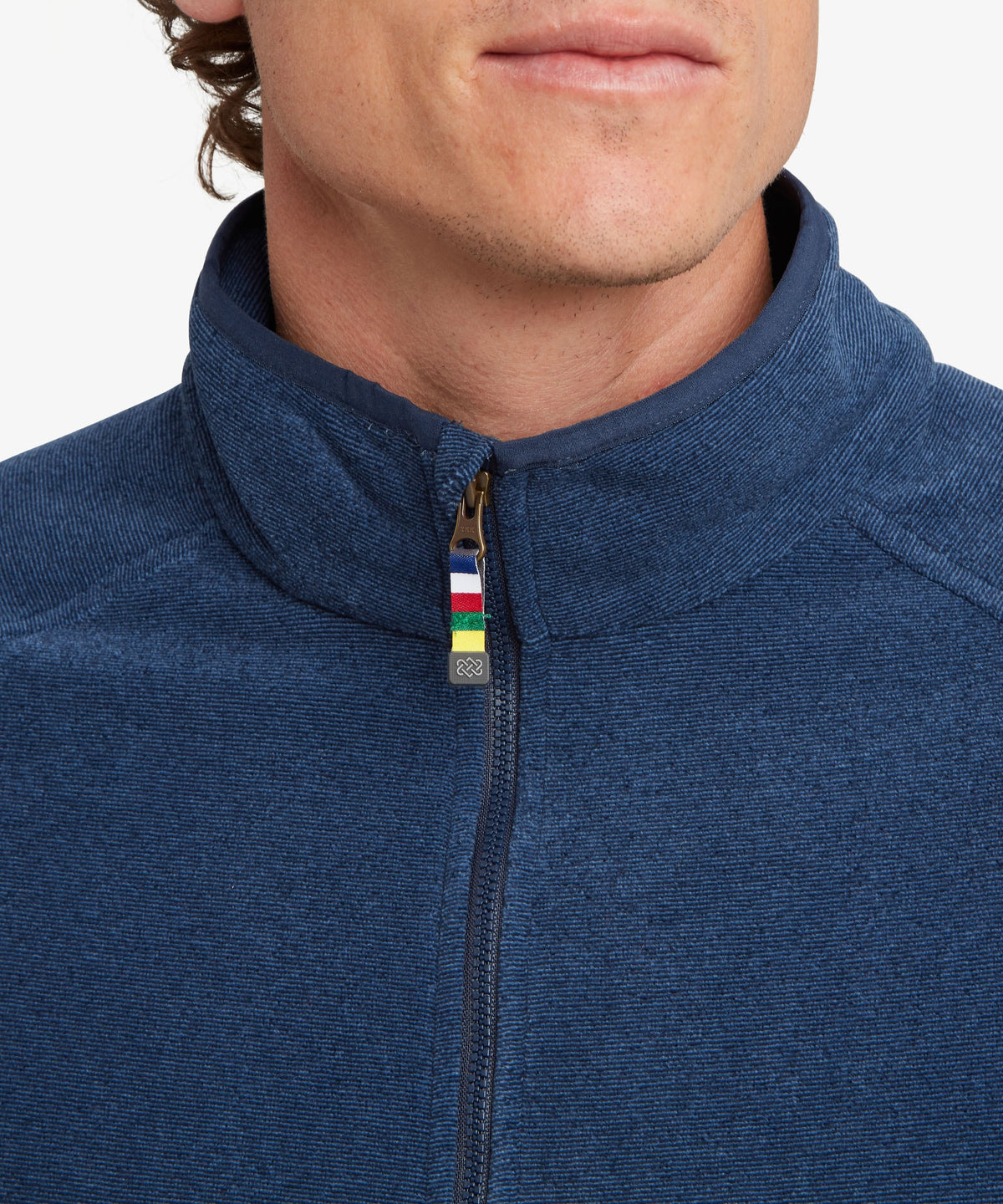Close-up of a man wearing a heathered blue quarter-zip pullover with a small multicolor prayer.