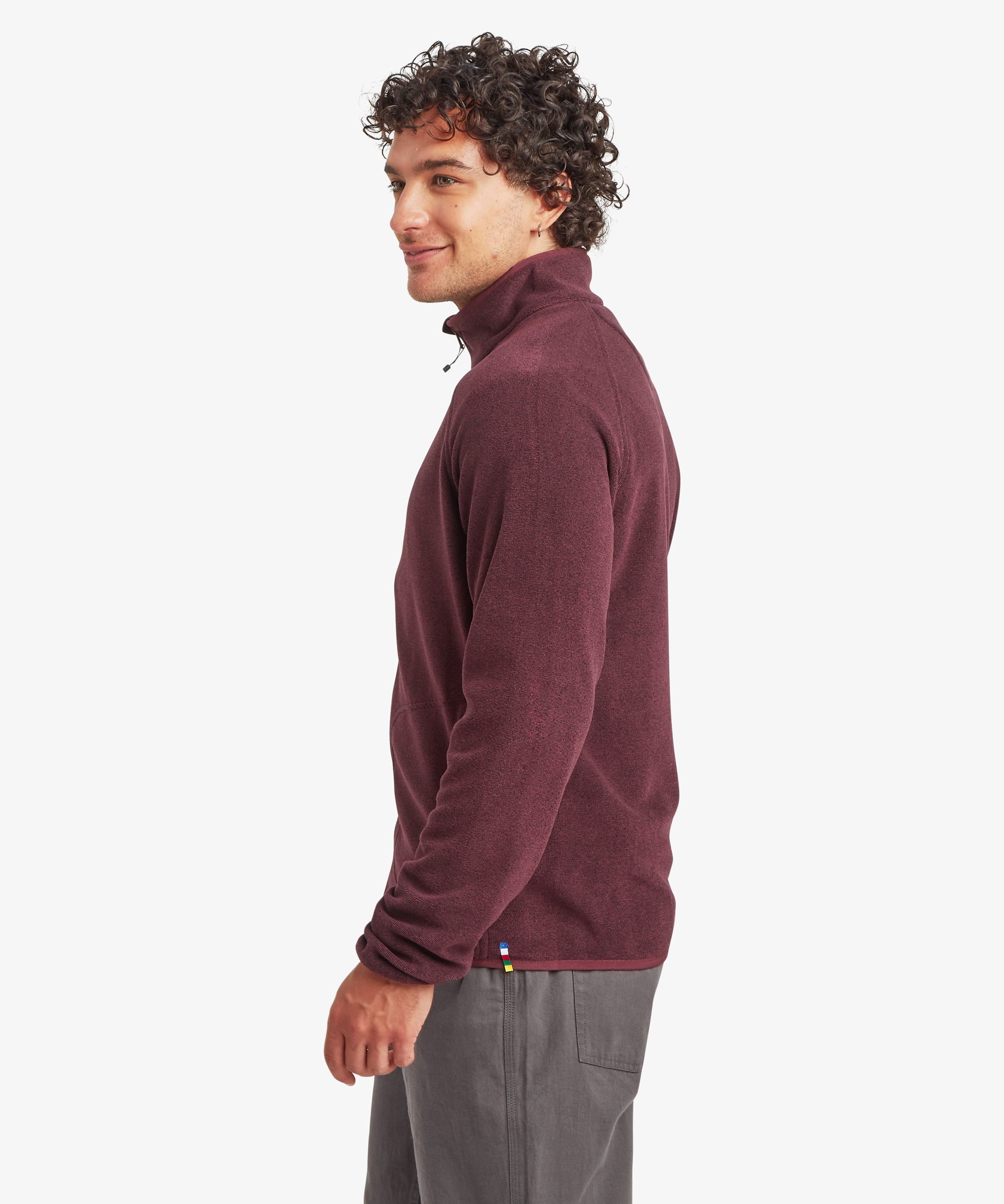 Side-profile view of the burgundy fleece jacket, highlighting the stand collar, streamlined silhouette, and soft textured fabric. Paired with grey pants.