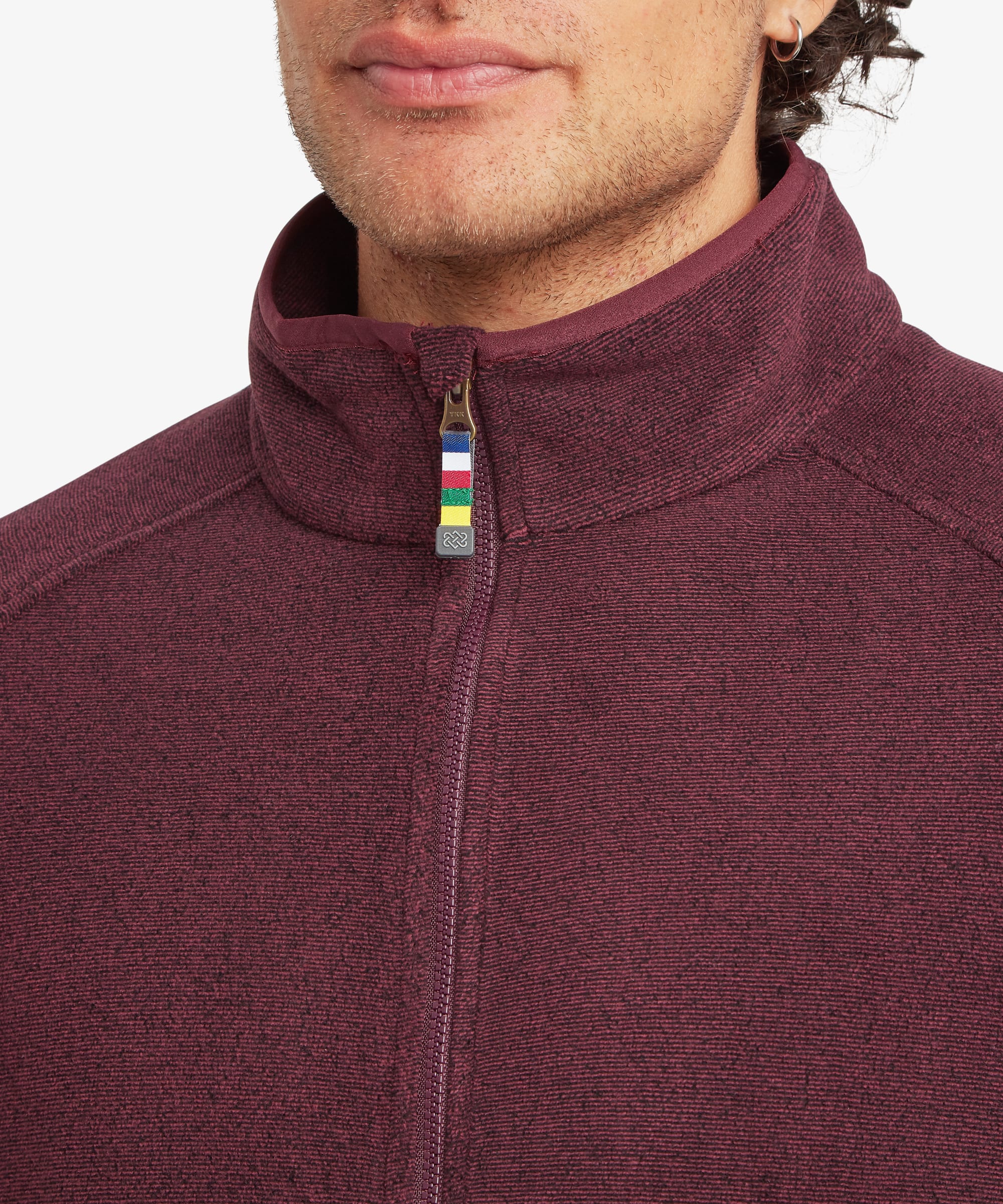 Close-up of the burgundy fleece jacket collar and full-length zipper. The stand collar features a multicolor striped accent tab at the zipper, with soft fleece texture visible throughout.