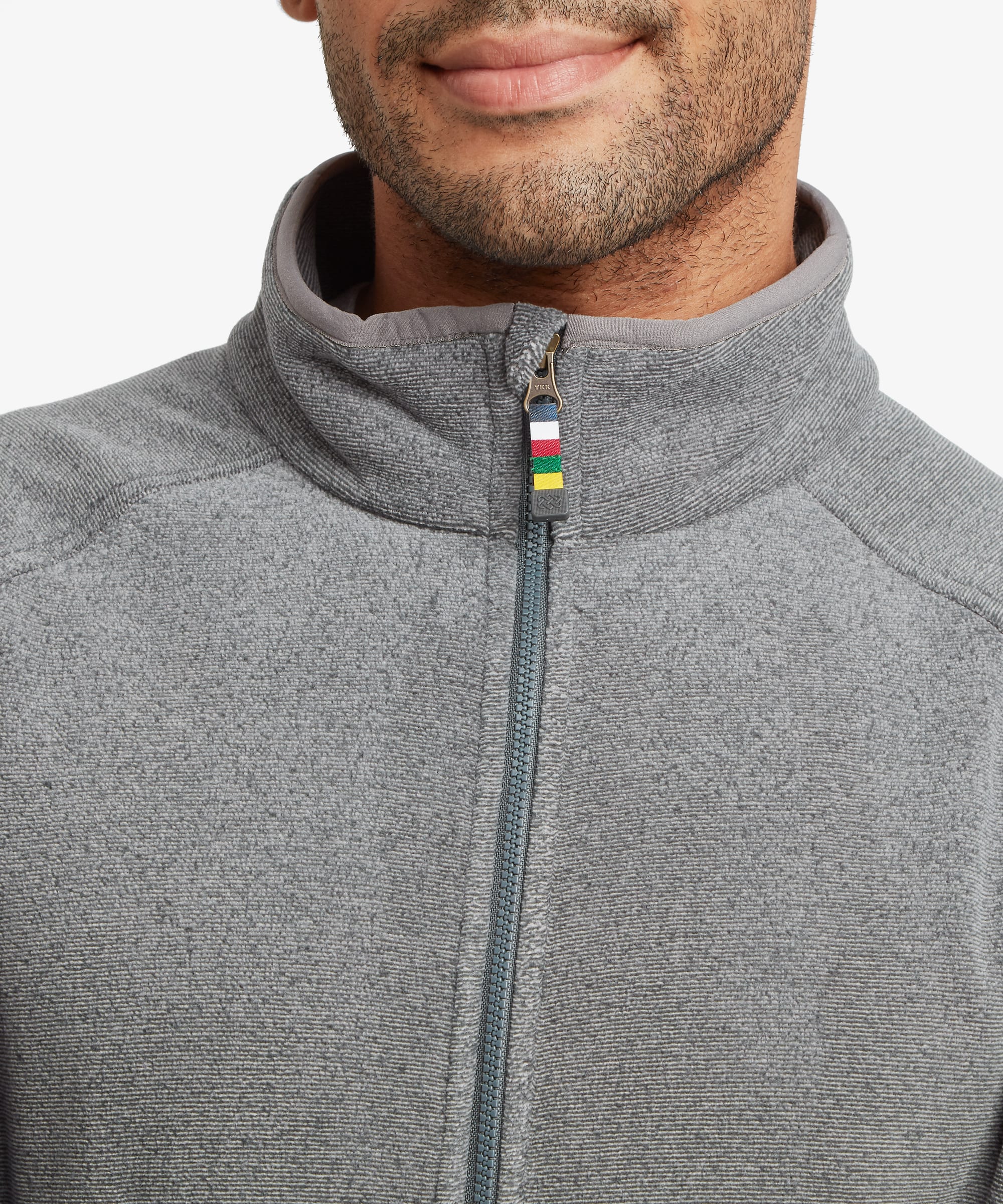Close-up of a man wearing a heather gray full zip fleece jacket with a high collar and a small multicolor zipper pull.