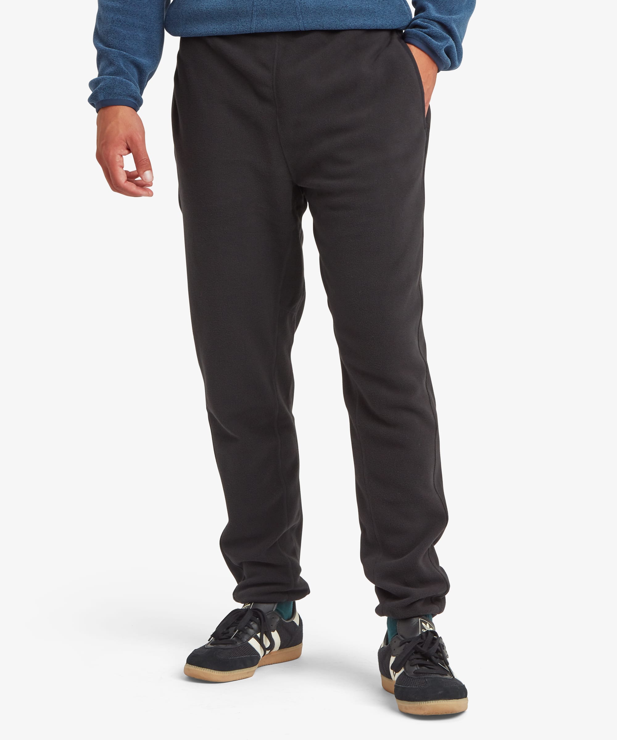 Front view of black fleece jogger pants featuring an elastic waistband, tapered legs, side pockets, and ribbed ankle cuffs. Styled with athletic shoes and a blue fleece pullover.