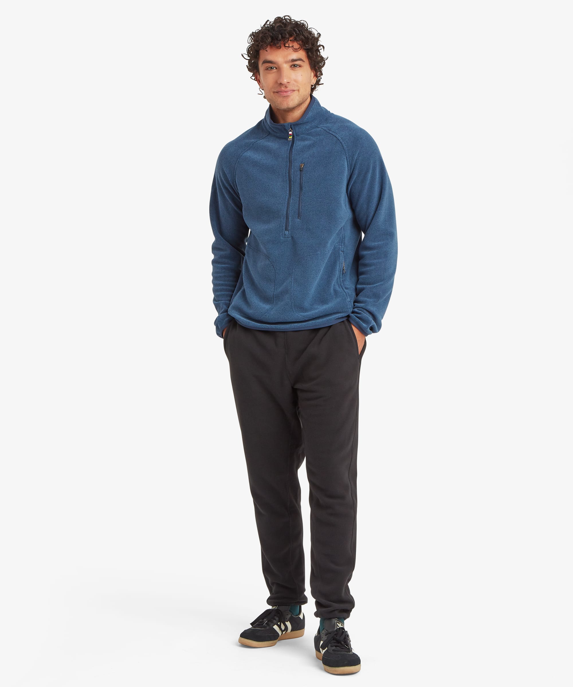 Full-body front view of a man wearing black fleece joggers with a tapered fit and elastic waistband. The joggers are paired with a blue quarter-zip fleece and black sneakers.
