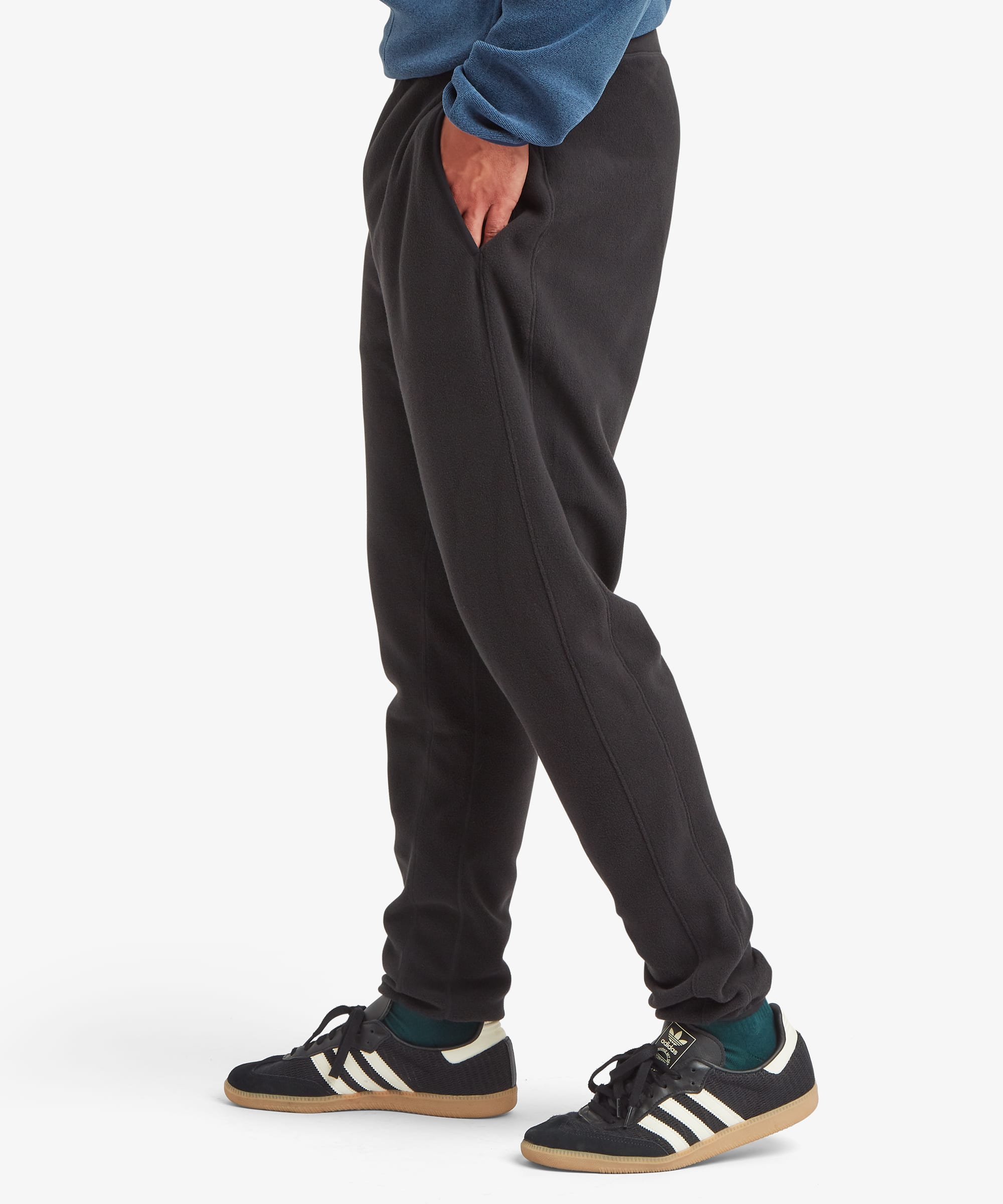 Side-profile view of black fleece joggers showing the slim tapered silhouette, ribbed cuffs, and relaxed fit through the hips and thighs.