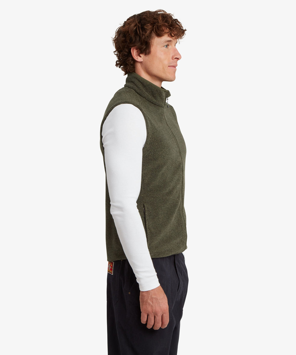 A man in profile wearing an olive green quarter-zip fleece vest over a white long-sleeve shirt.