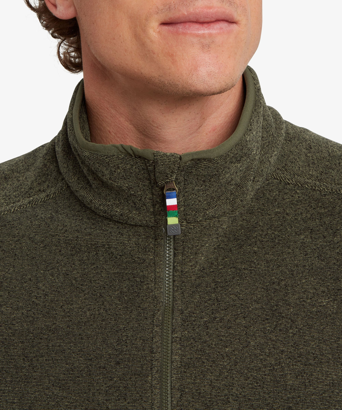 Close-up of a man wearing an olive green half-zip fleece pullover with a small multicolor prayer.