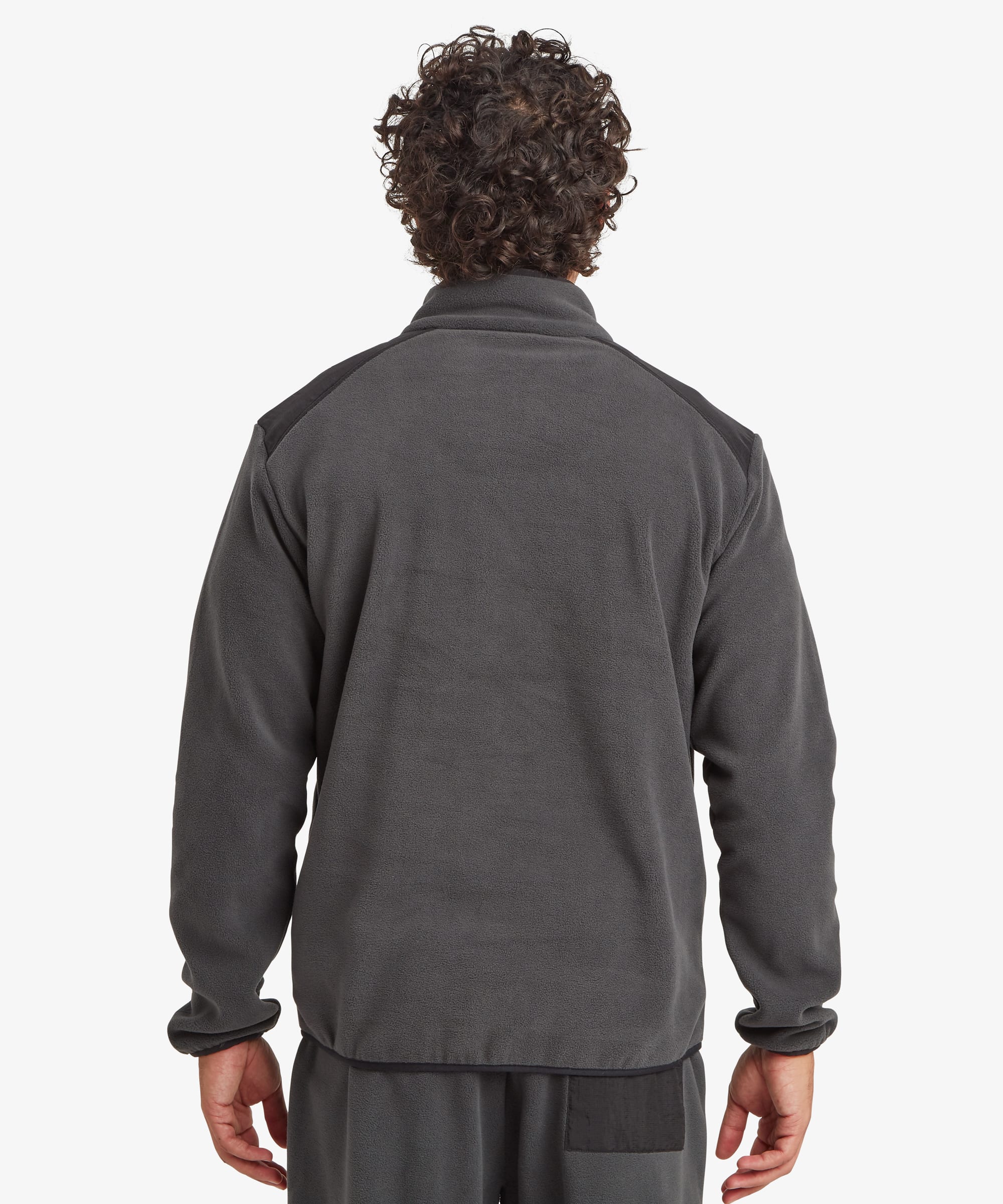 Back view of a man wearing a black Sanu 1/2-zip fleece pullover. The jacket features a stand collar, clean rear design, and relaxed fit through the shoulders and body. Styled with blue jeans.
