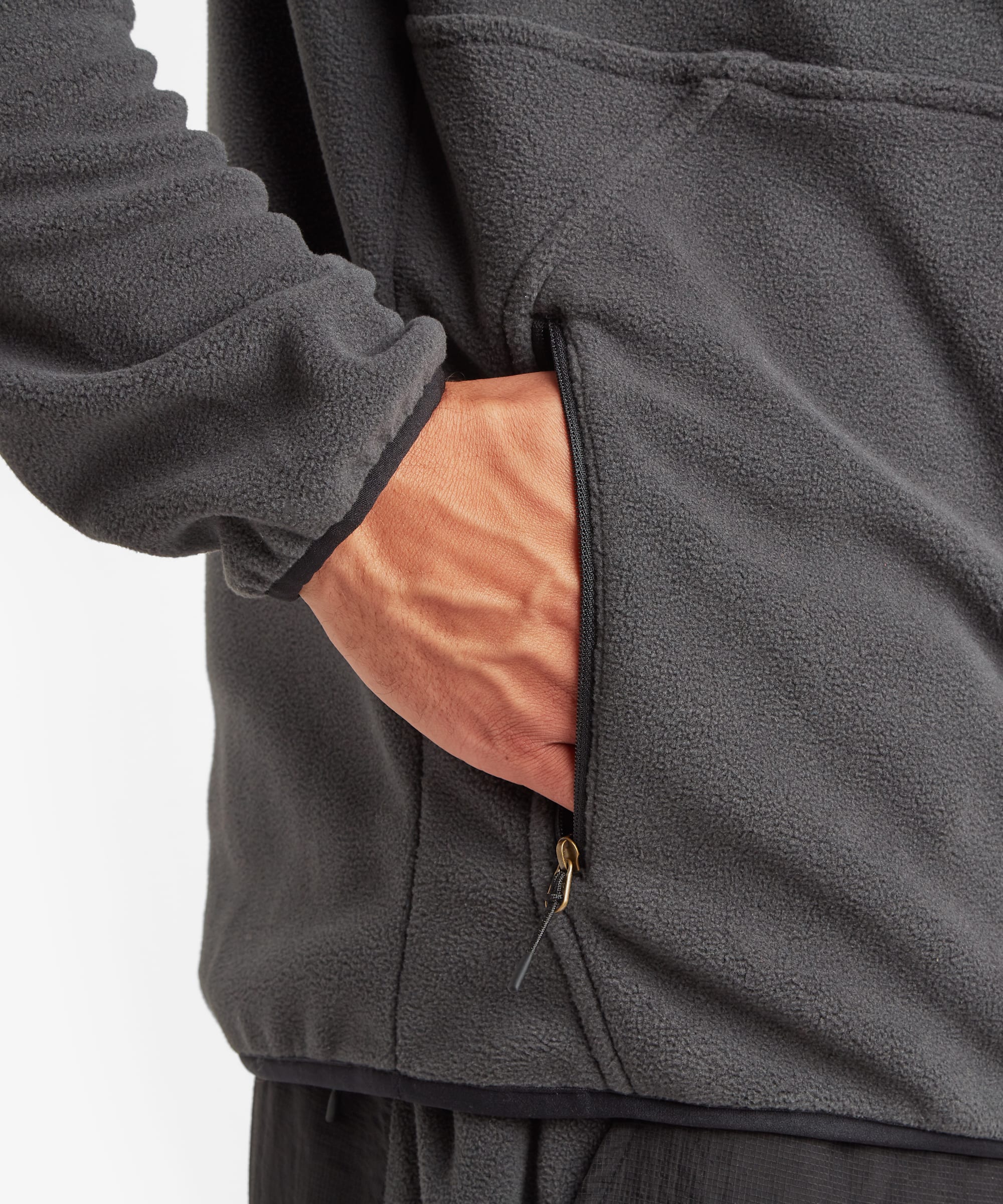 Close-up detail of the black fleece pullover showing a zippered hand pocket, soft fleece texture, and a hand placed inside the pocket to demonstrate storage capacity.