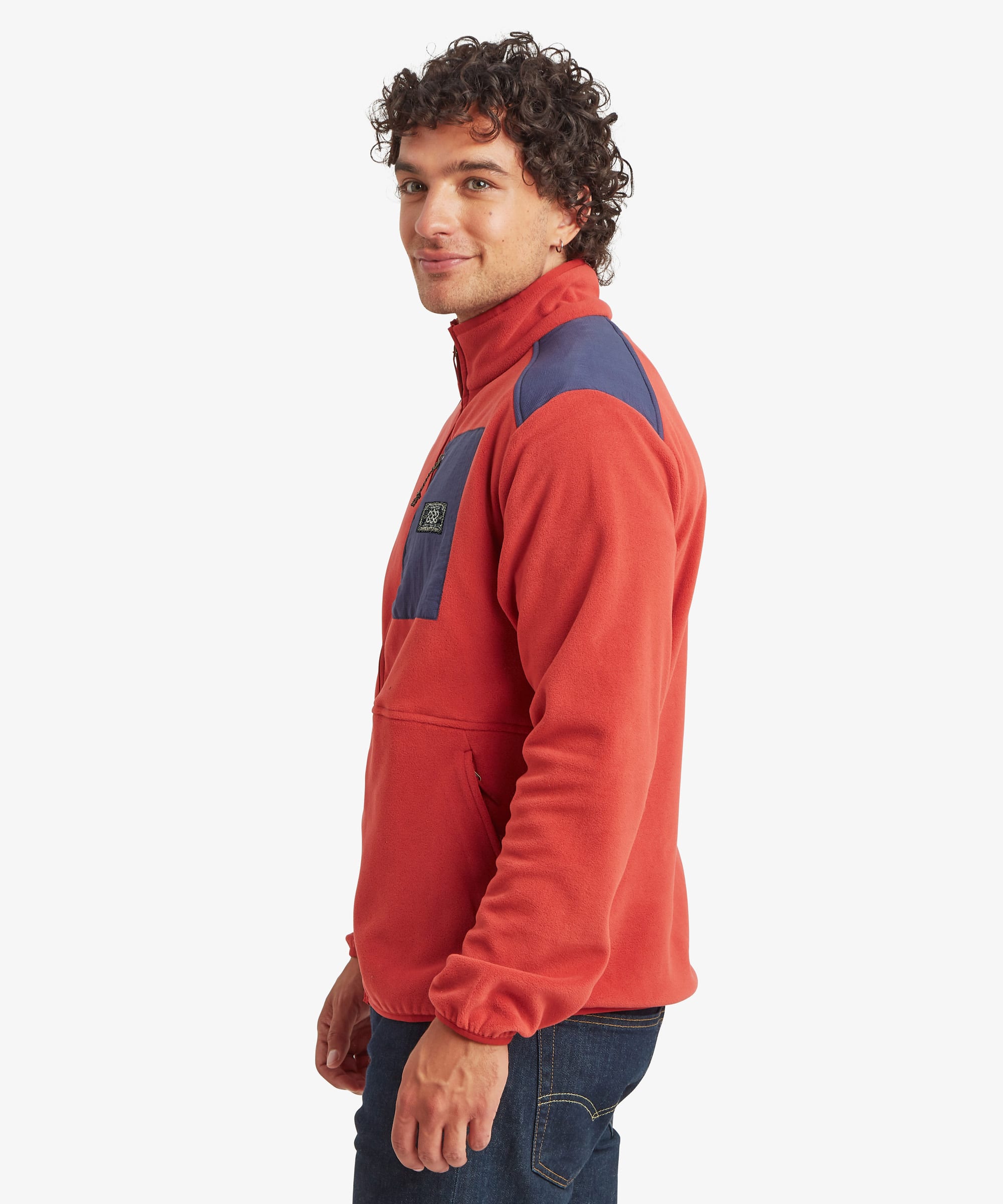 Side profile of a male model wearing the Sherpa Sanu Full Zip in red with navy shoulder and chest pocket panels, showing the relaxed fit, high collar, long sleeves and the soft fleece texture.