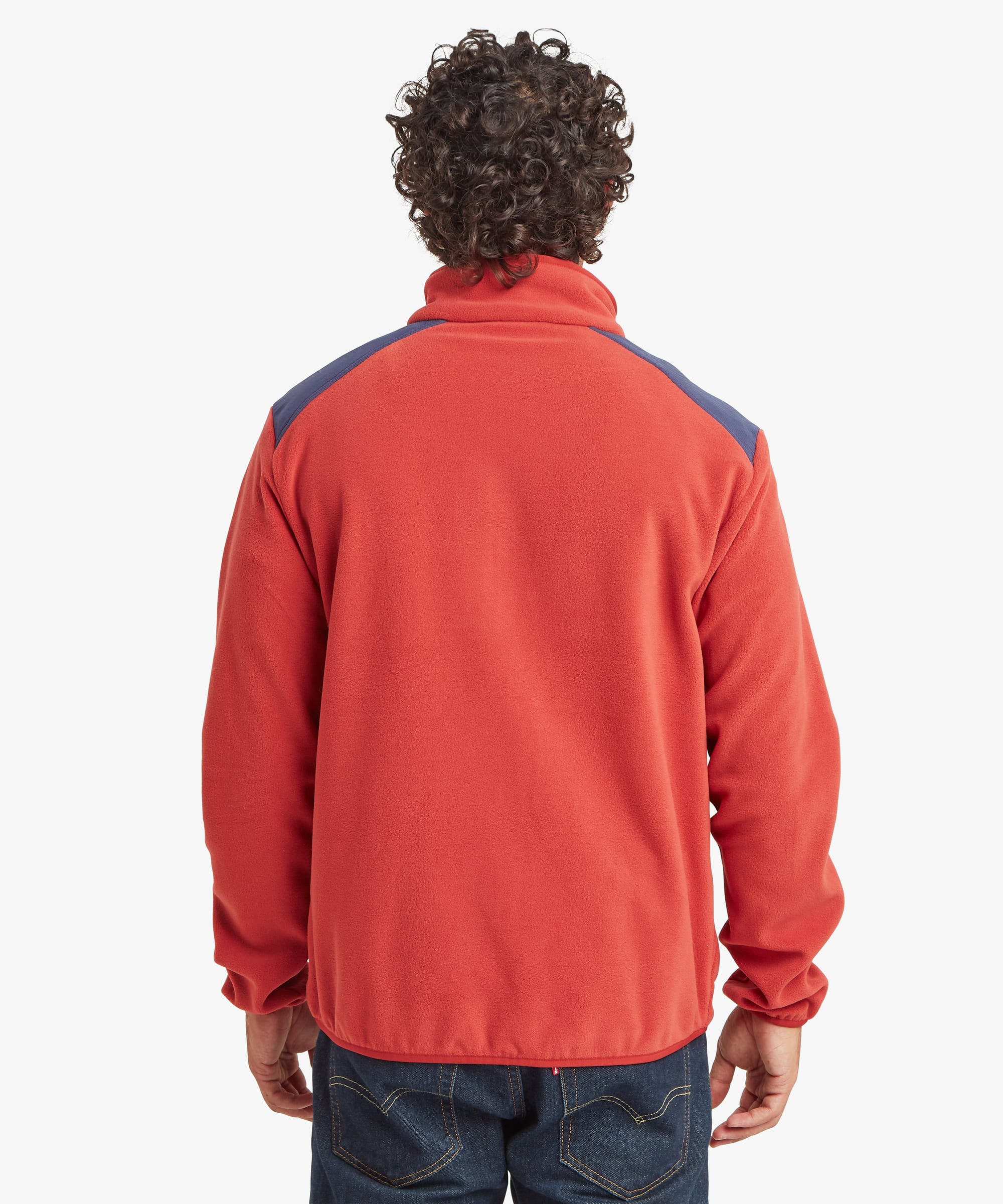 Rear view of a male model wearing the Sherpa Sanu Full Zip in red with navy shoulder panels, displaying the clean back design, stand collar, elasticated hem and relaxed fit through the body and sleeves.