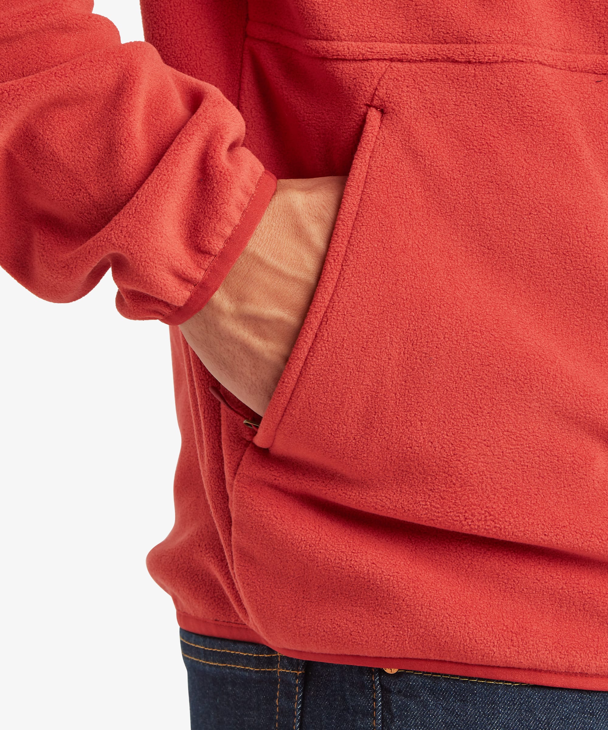 Close-up of the red fleece jacket showing a zippered hand pocket, soft fleece texture, and a hand resting inside the pocket.
