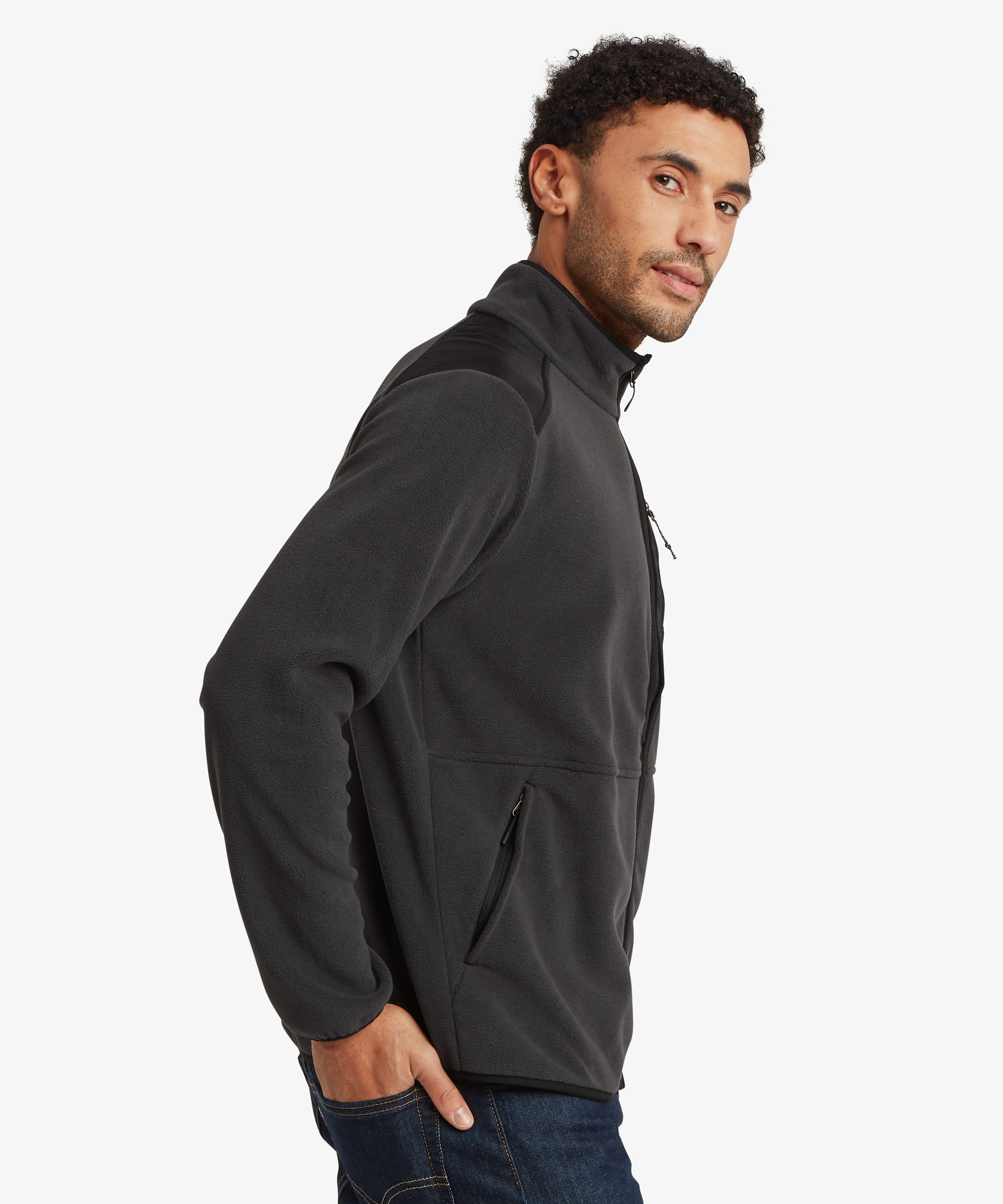 Side-profile view of a man wearing a black full-zip fleece jacket with a stand collar and zip-front closure. The jacket has a relaxed fit and is paired with blue jeans.