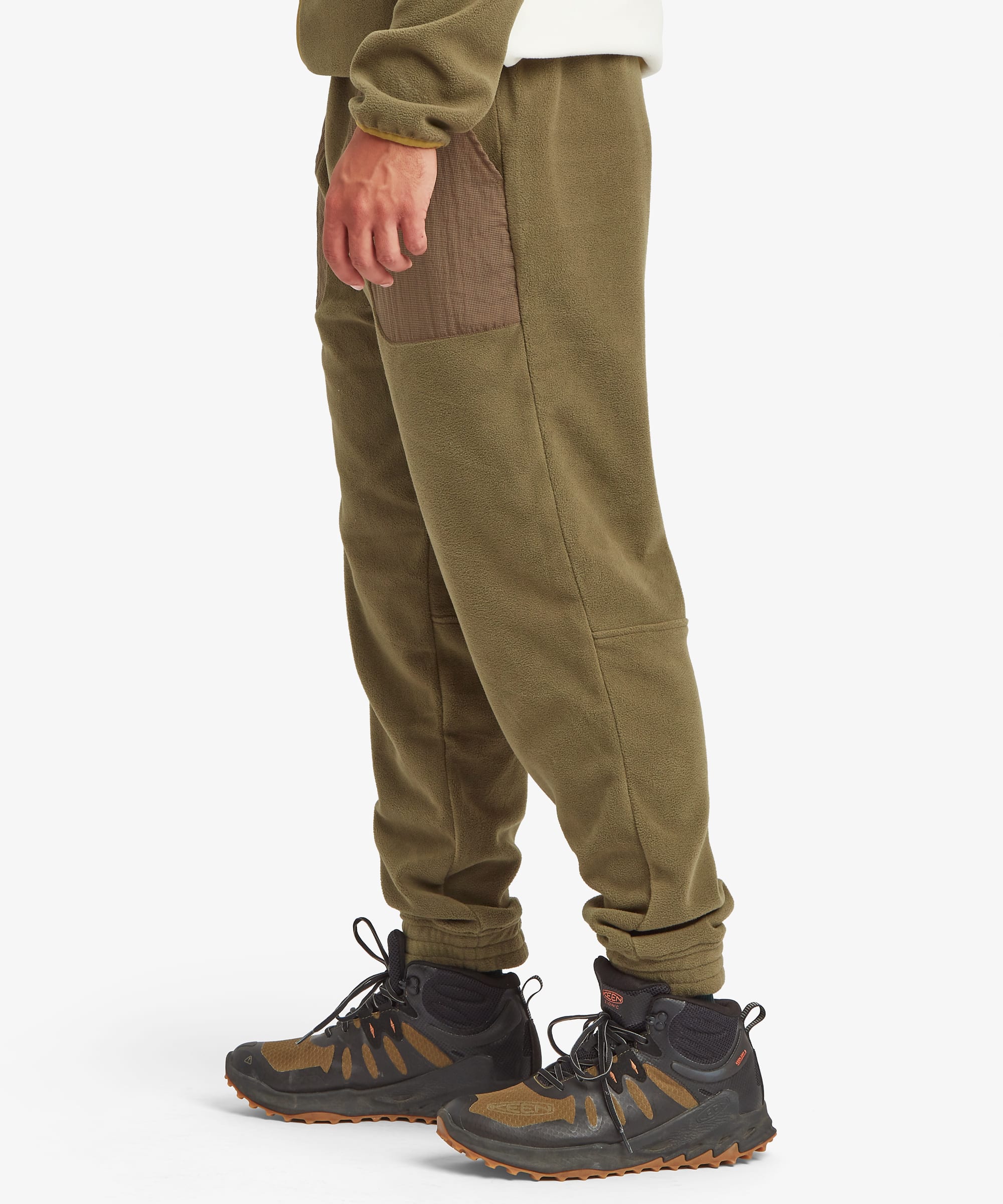 Side profile of olive green jogger pants highlighting the tapered leg, elastic ankle cuffs, and large contrast patch pocket positioned on the outer thigh.