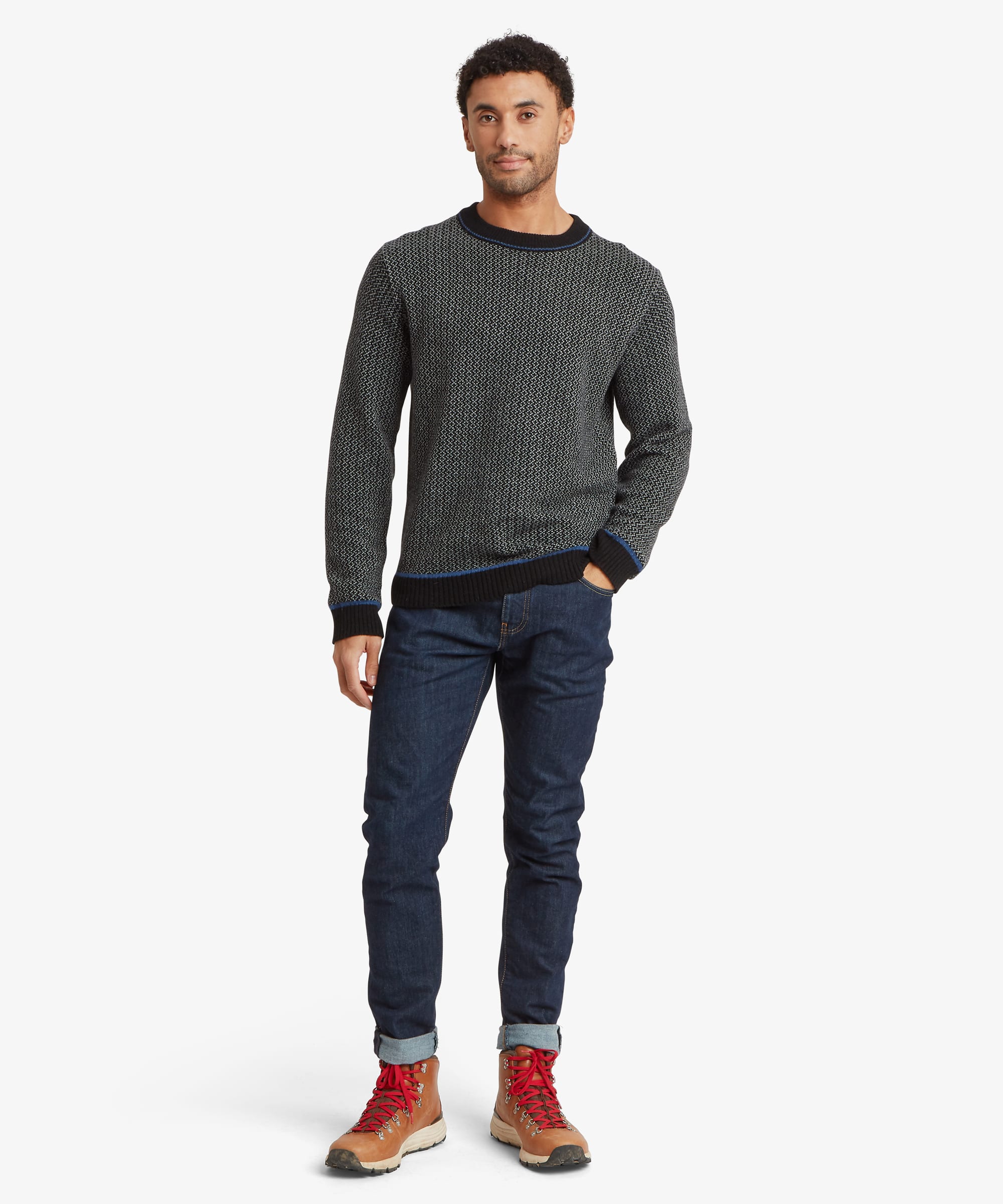 Full-body front view of a model wearing a charcoal grey textured knit crew neck sweater with ribbed trims and a subtle logo tab at the hem.