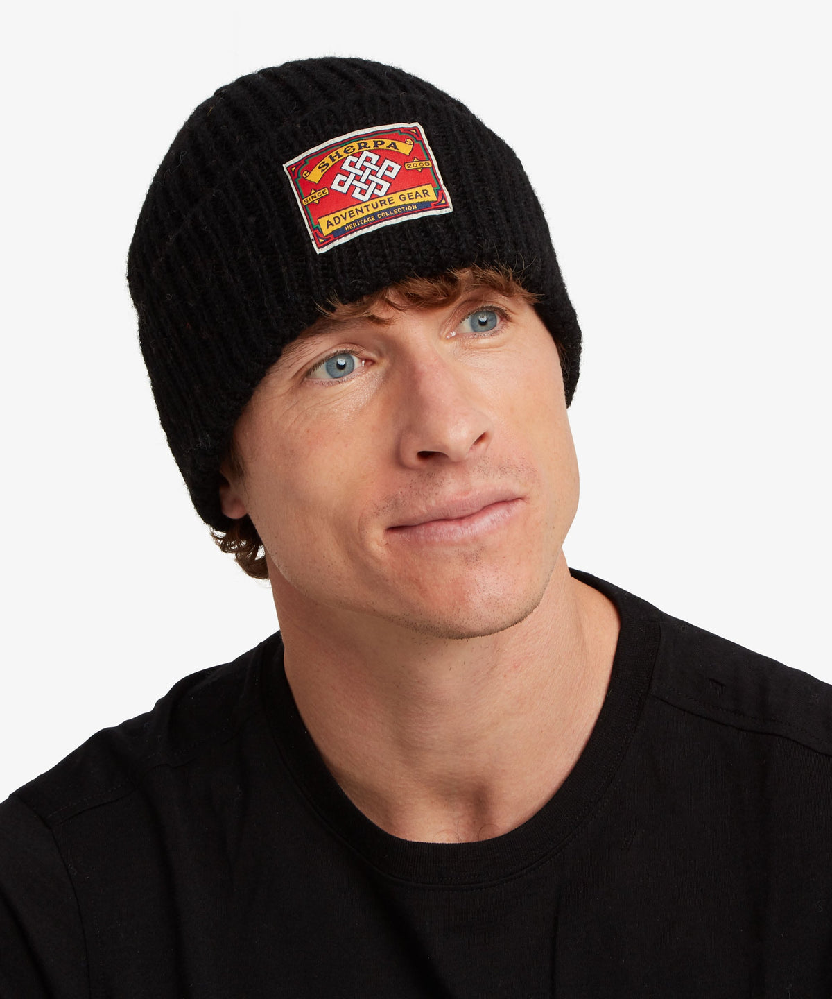 A man wearing a black knit beanie with a red and yellow embroidered patch on the front.