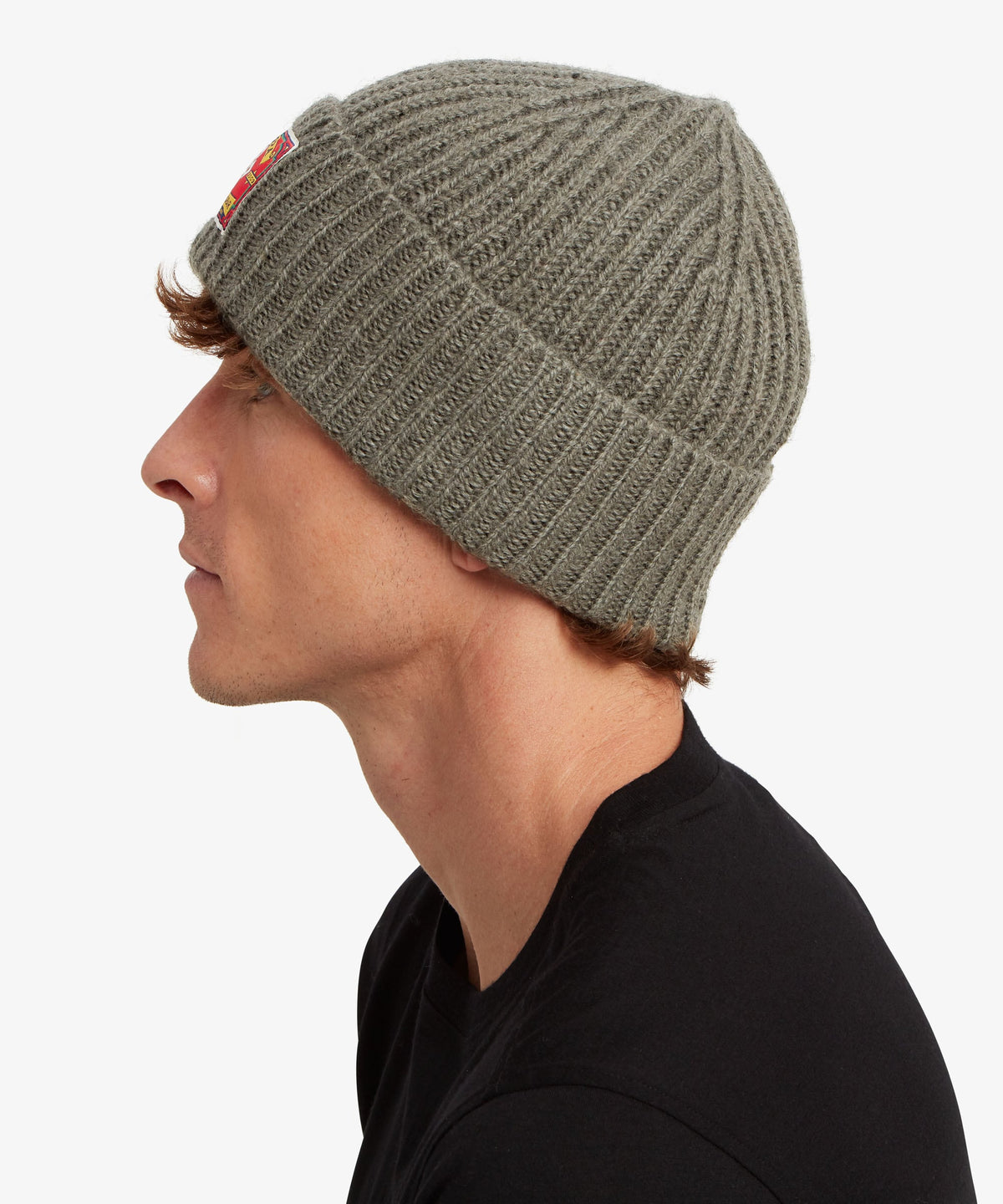 A man in profile wearing a ribbed knit beanie hat in a muted olive green color.