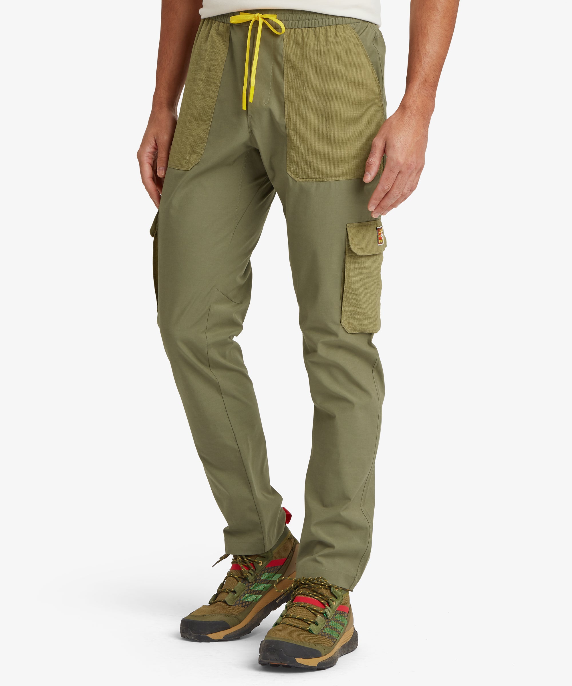 Full‑body view of olive technical cargo pants worn with trail shoes, highlighting the paneled fabric design, secure pockets, and tapered outdoor‑ready silhouette.