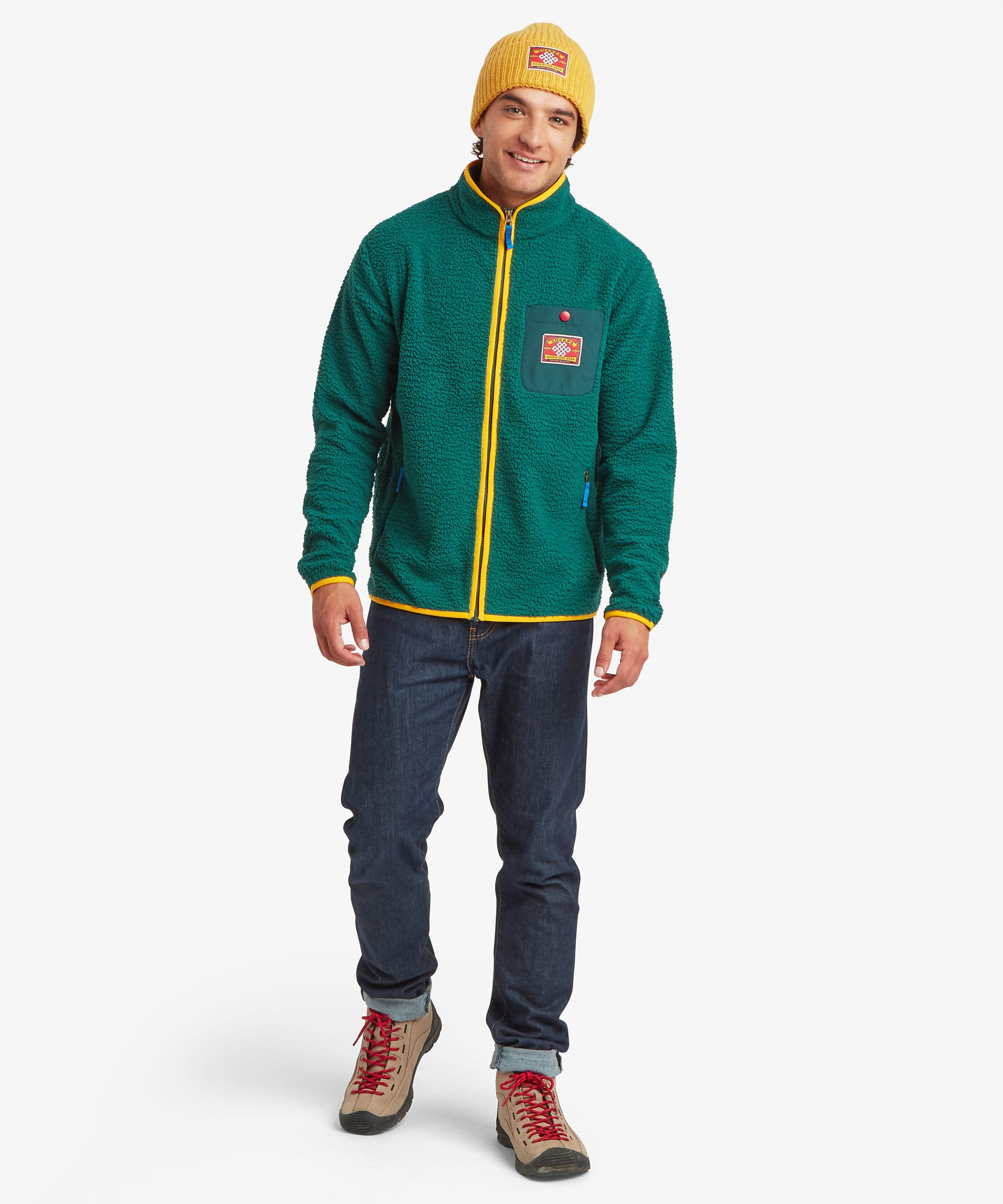 Full-body front view of a model wearing a green fleece jacket with yellow zipper accents, zippered pockets, stand collar, and a colorful logo patch on the chest pocket.