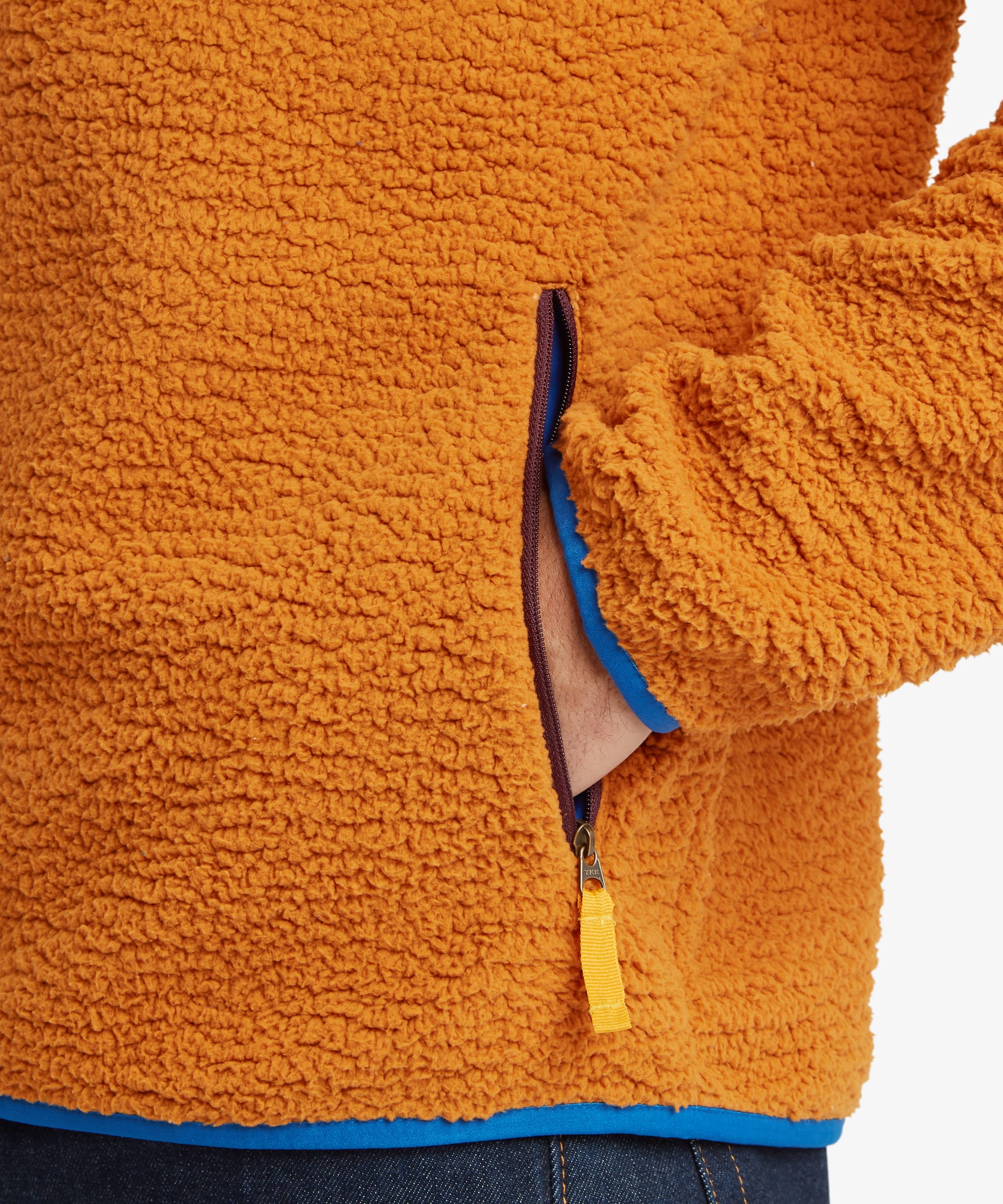 Close-up of the jacket’s zippered hand pocket with contrasting blue zipper tape, showcasing the textured sherpa fleece fabric and functional storage feature.