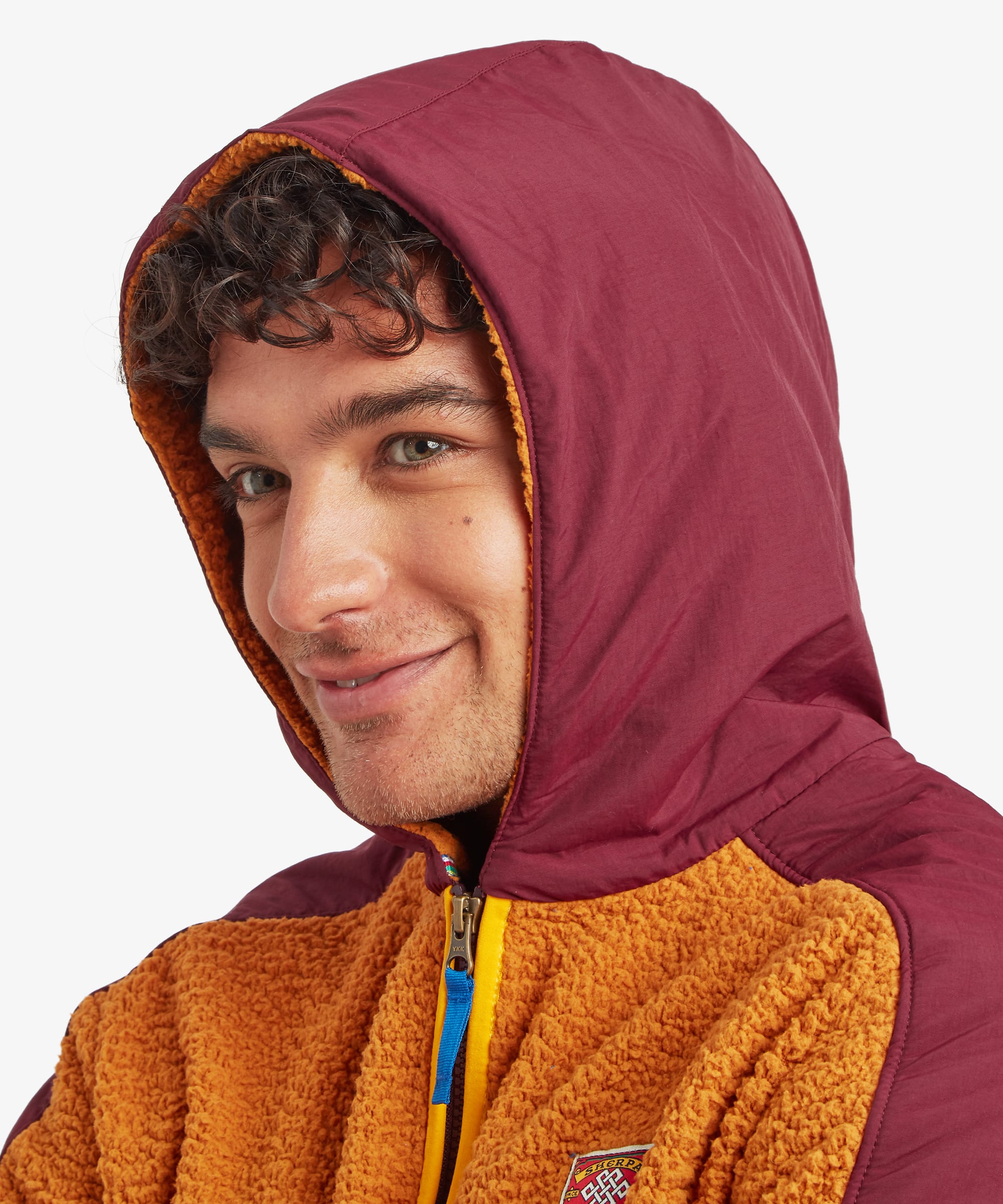 Close-up of a male model wearing the yellow Sherpa Tarcho Hooded Jacket with the hood up, highlighting the soft fleece texture, high collar and contrasting hood. The jacket also features yellow contrast binding on the zip, a blue zip puller and a patch with the Sherpa Adventure Gear logo.