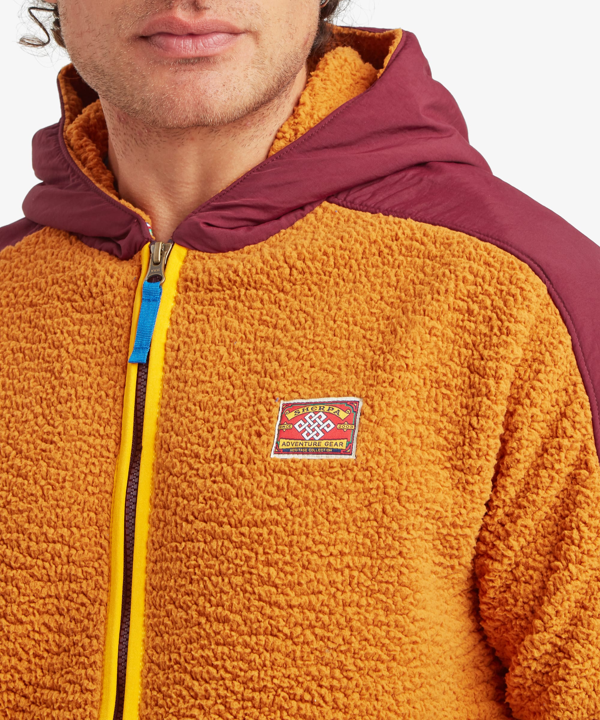 Close-up of the yellow Sherpa Tarcho Hooded Jacket worn by a male model, showcasing the soft high-pile fleece, full-length zip, embroidered Sherpa logo patch and contrasting hood.