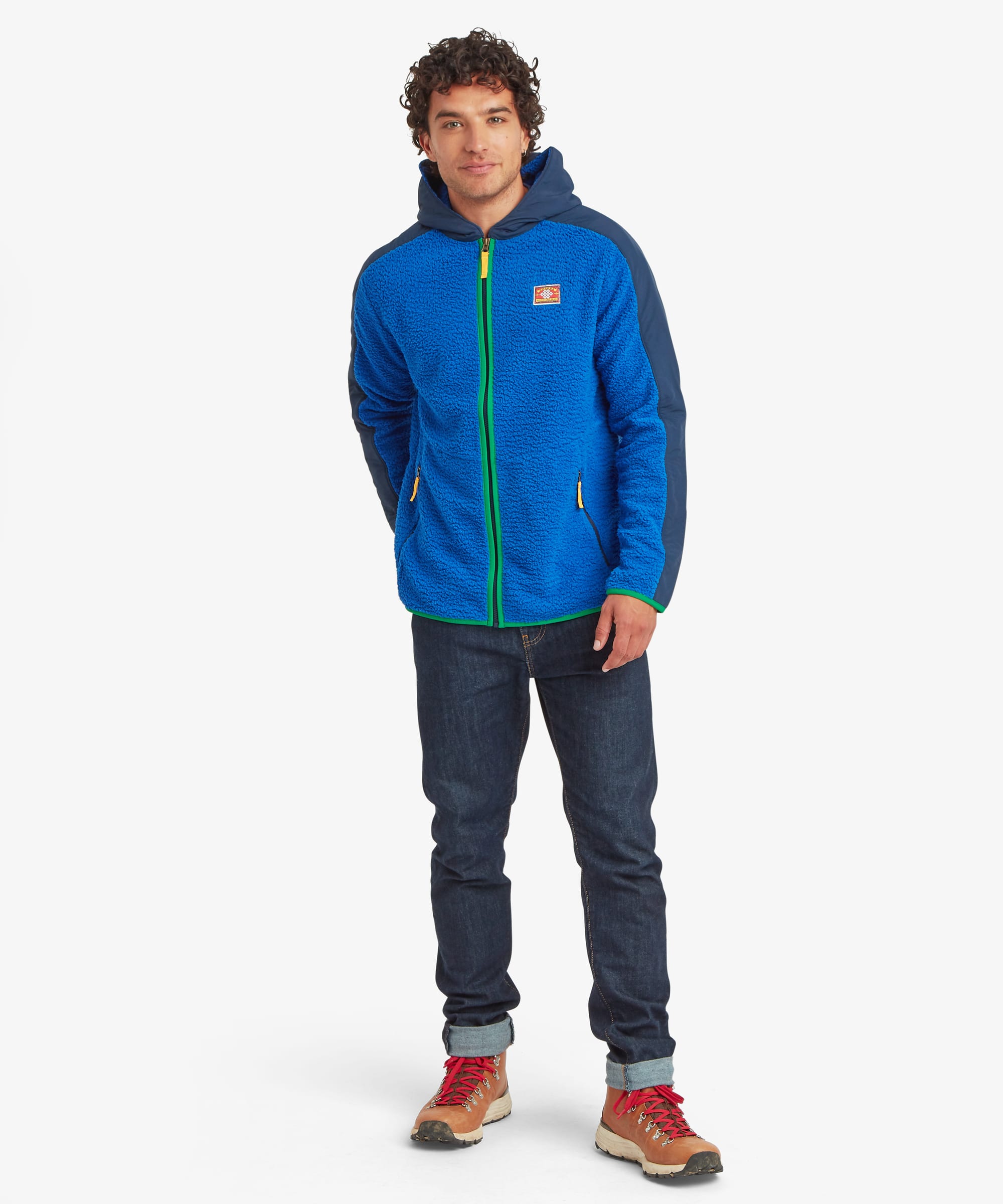 Full-length front view of a male model wearing the blue Sherpa Tarcho Hooded Jacket, showing the relaxed fit, contrasting hood and sleeves, full-zip design and zipped pockets.