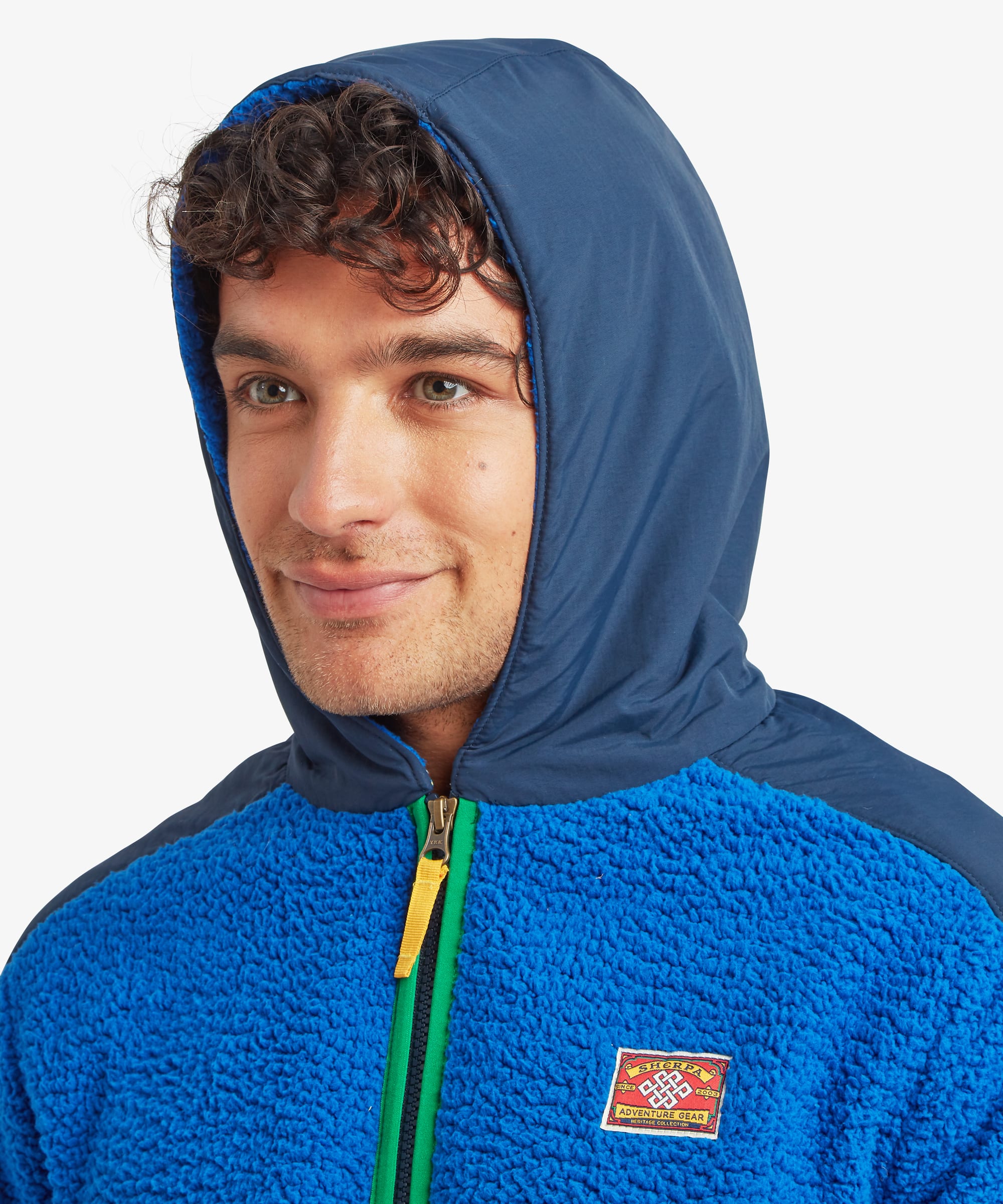 Close-up of a male model wearing the blue Sherpa Tarcho Hooded Jacket with the hood up, showcasing the soft fleece texture, high collar and contrasting hood.