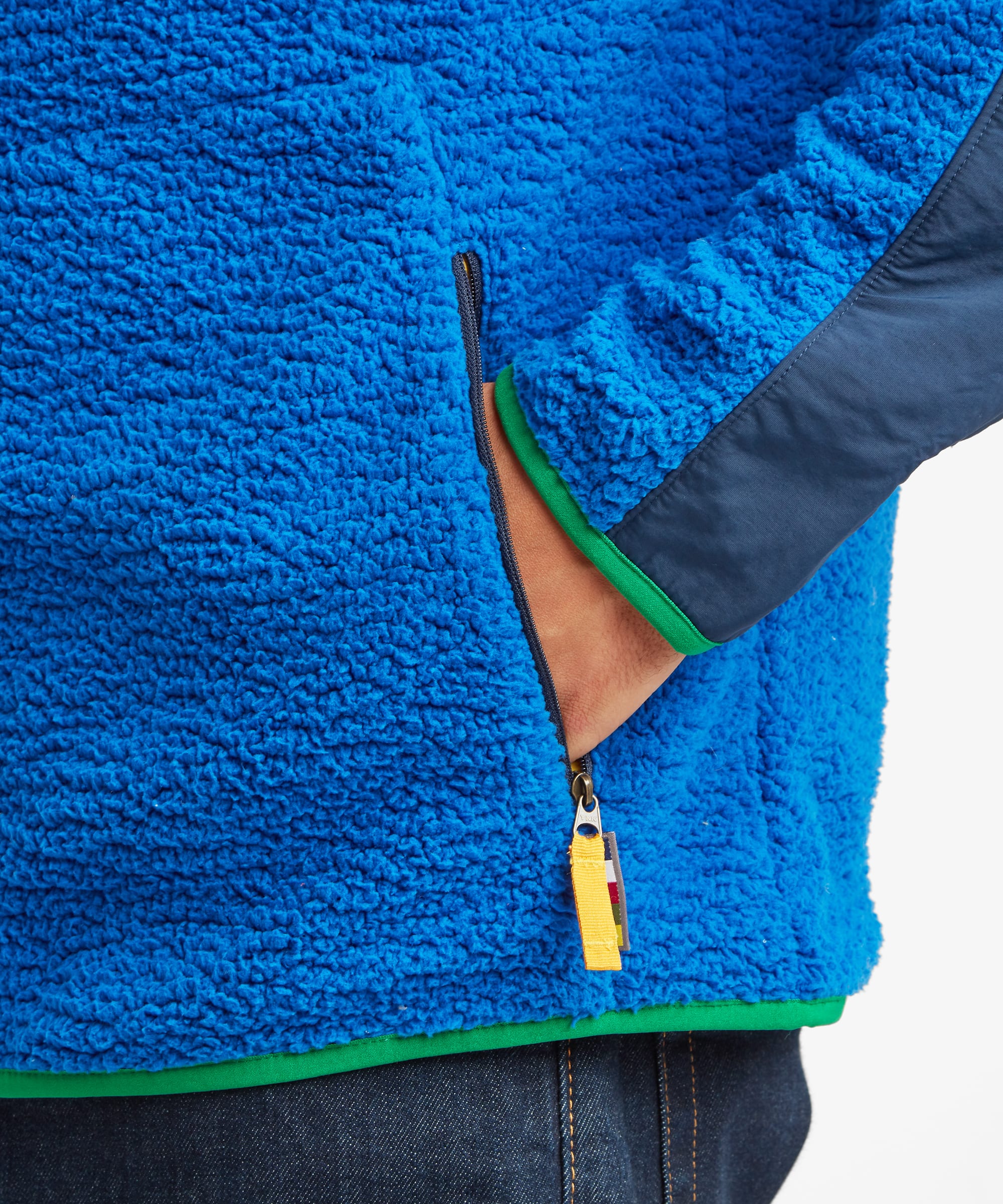 Close-up of the blue Sherpa Tarcho Hooded Jacket showing the zipped hand pocket, textured fleece fabric and contrasting trim on the hems and zip pullers.
