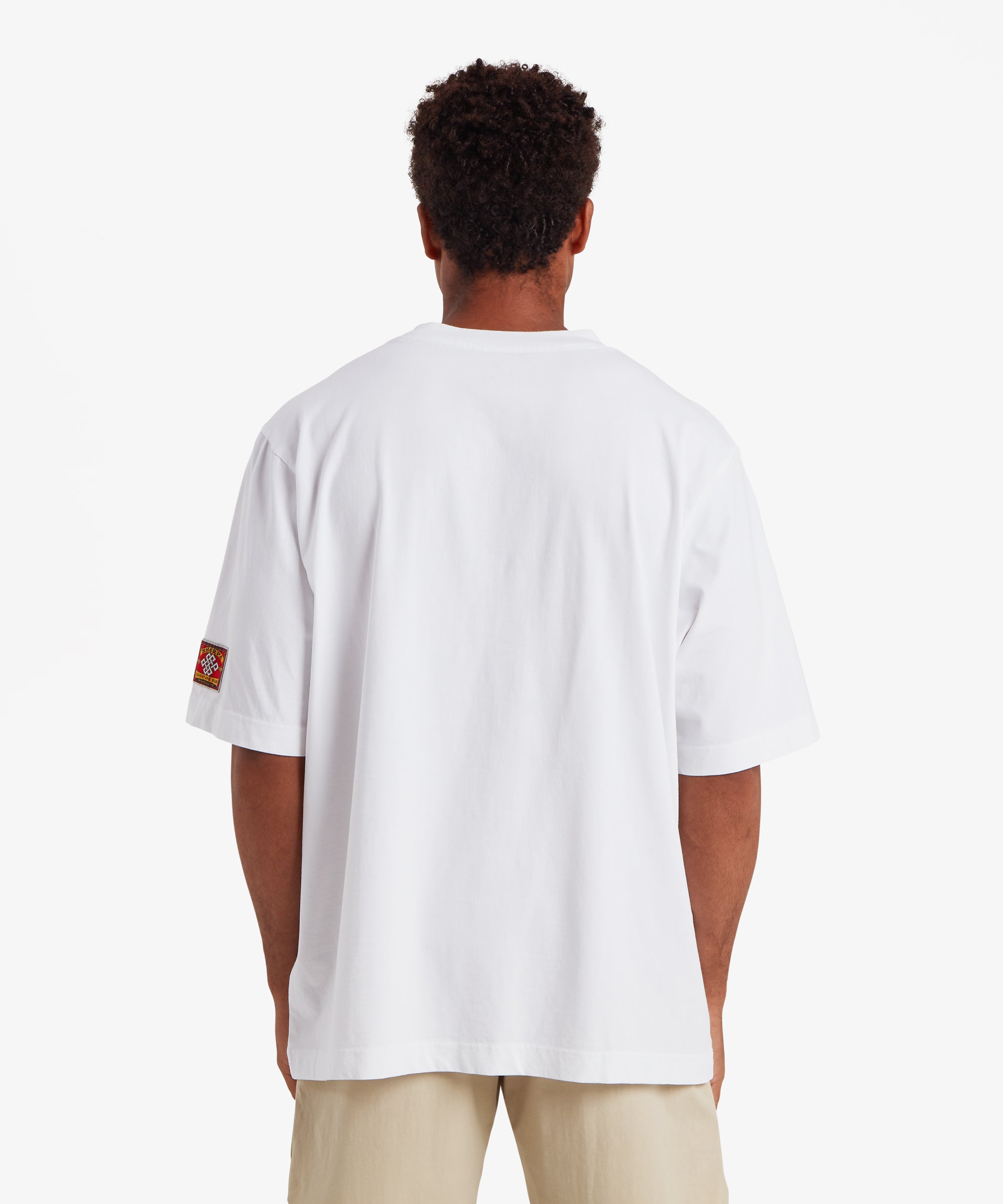 A back view of a man wearing relaxed fit white T-shirt. The T-shirt is plain of the man with no graphic or detail. The T-shirt is paired with beige shorts.